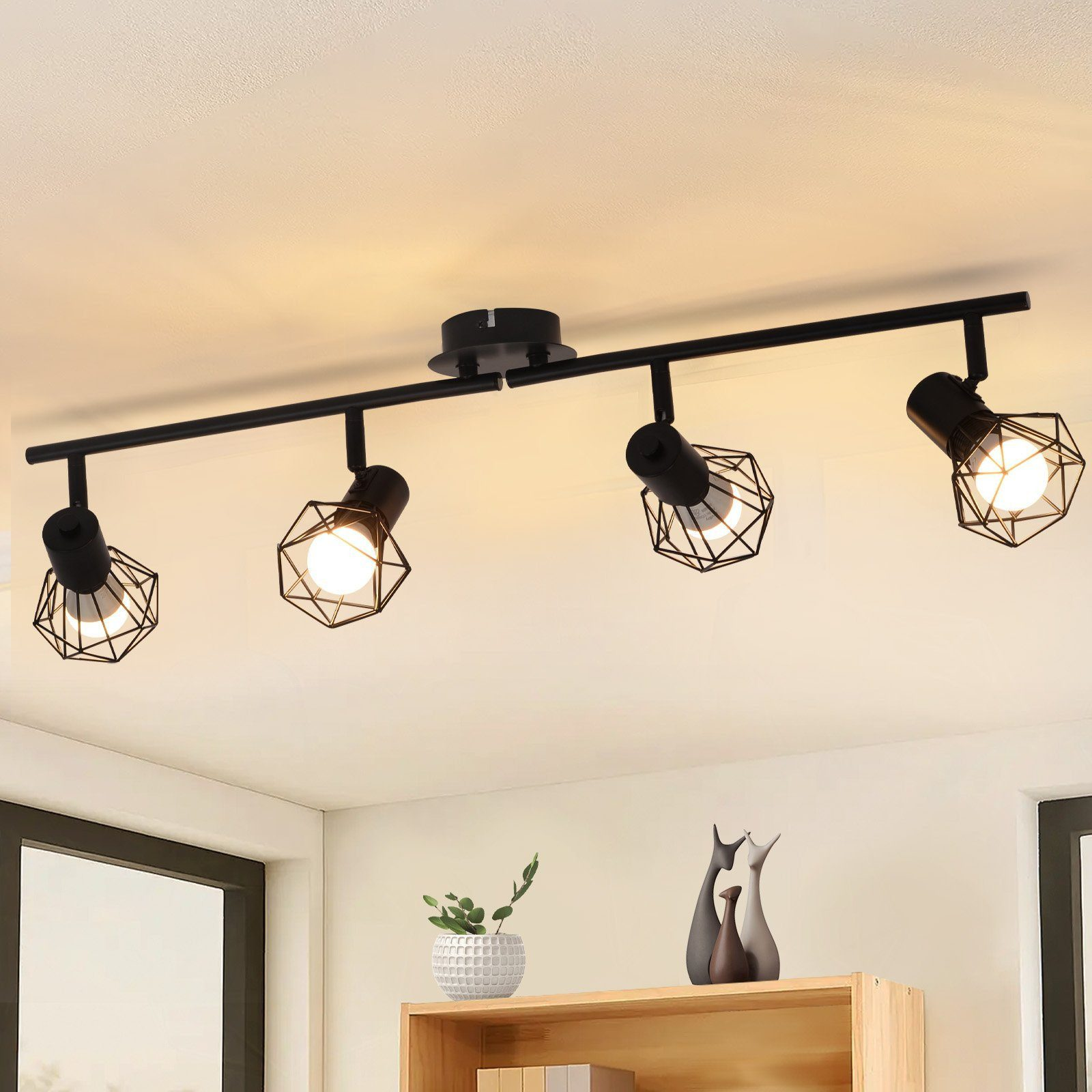 Czarny system oświetlenia szynowego z czterema regulowanymi reflektorami z kloszami z drutu na białym suficie.