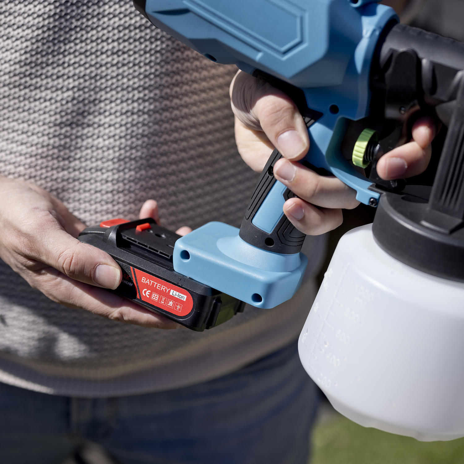 Persoon bevestigt een batterij aan een blauw en wit spuitpistool, buiten.