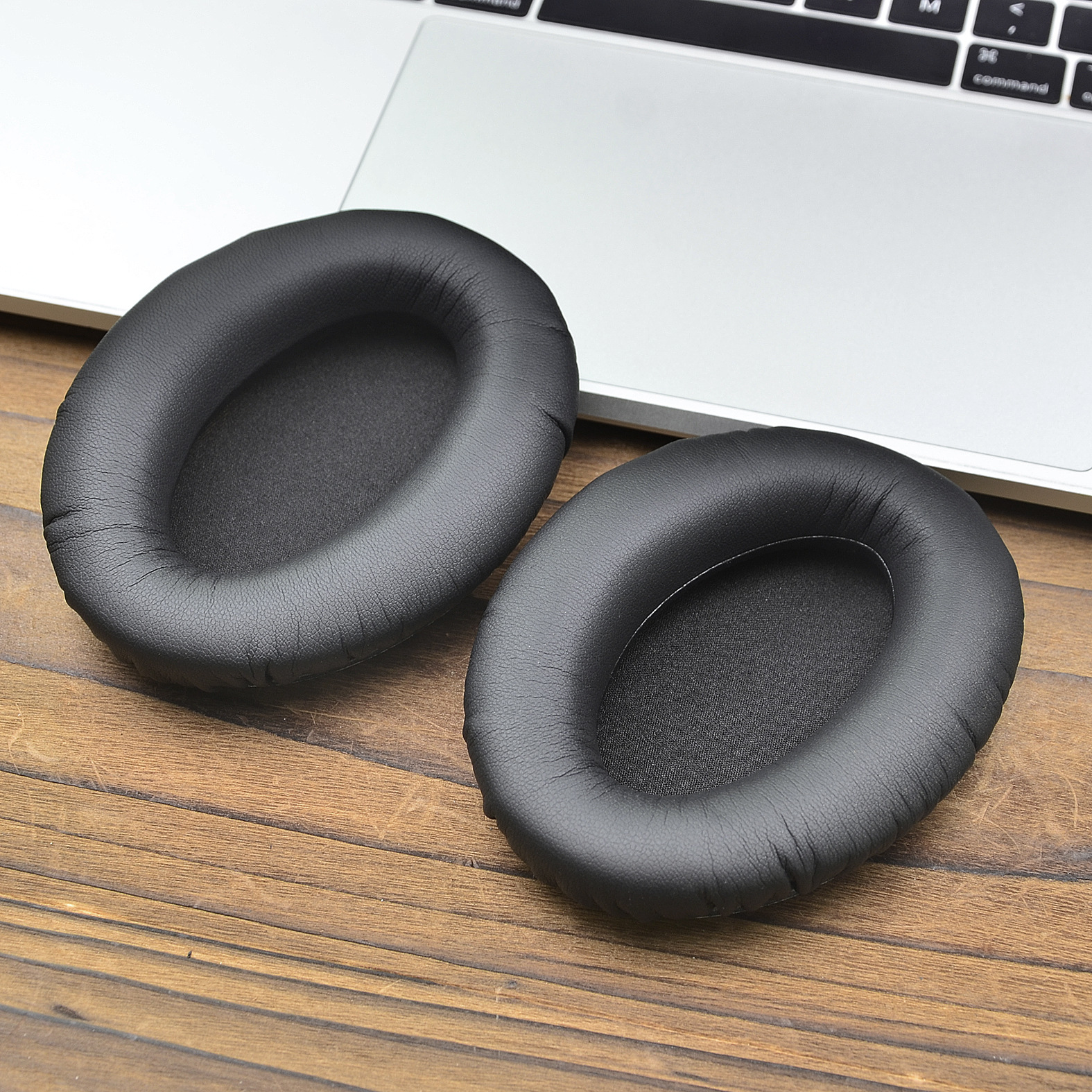 Cuscinetti auricolari neri su una superficie di legno, vicino a un computer portatile.