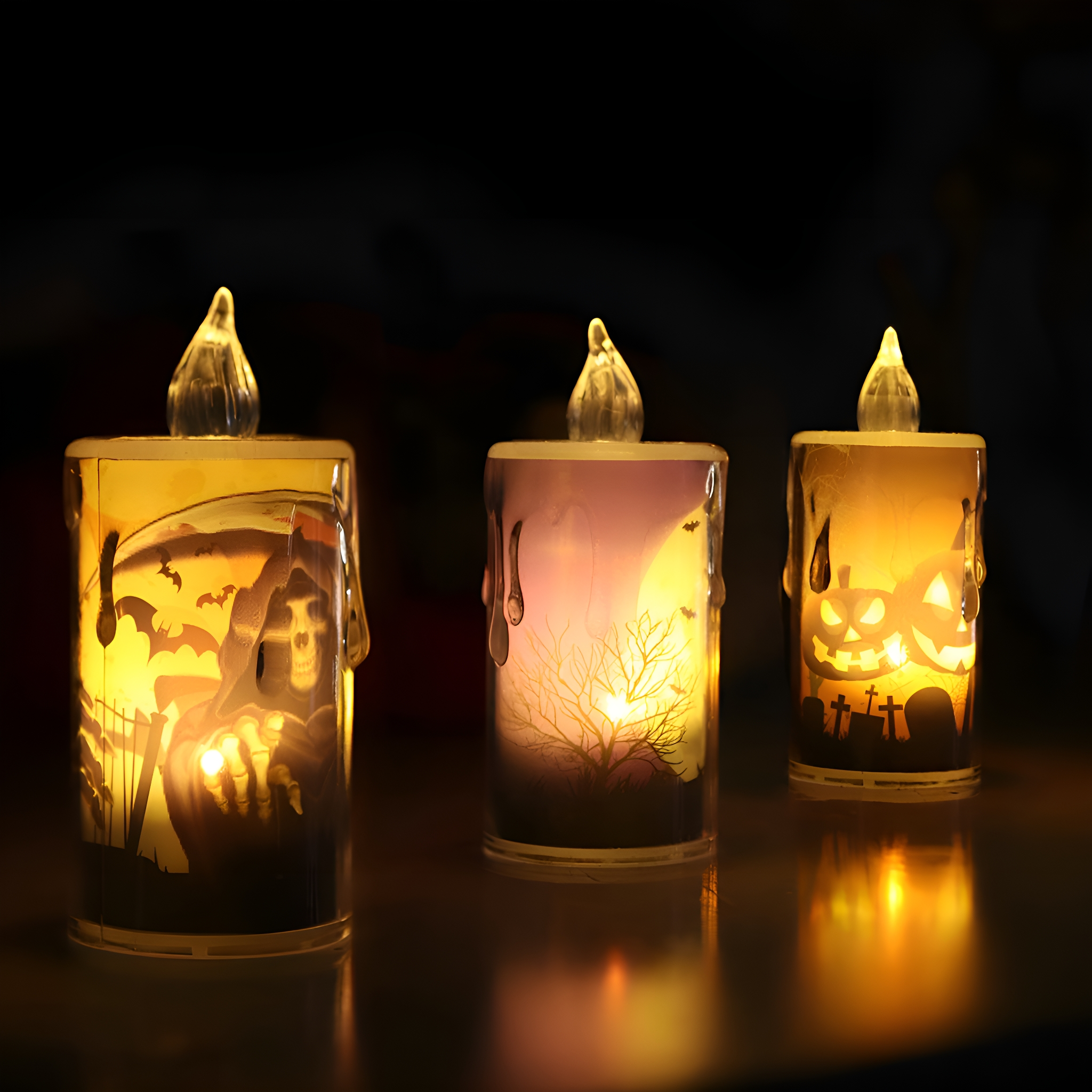 Drei Halloween-LED-Kerzen, jede mit einem anderen Design: ein Sensenmann, ein Mond und ein Kürbis.