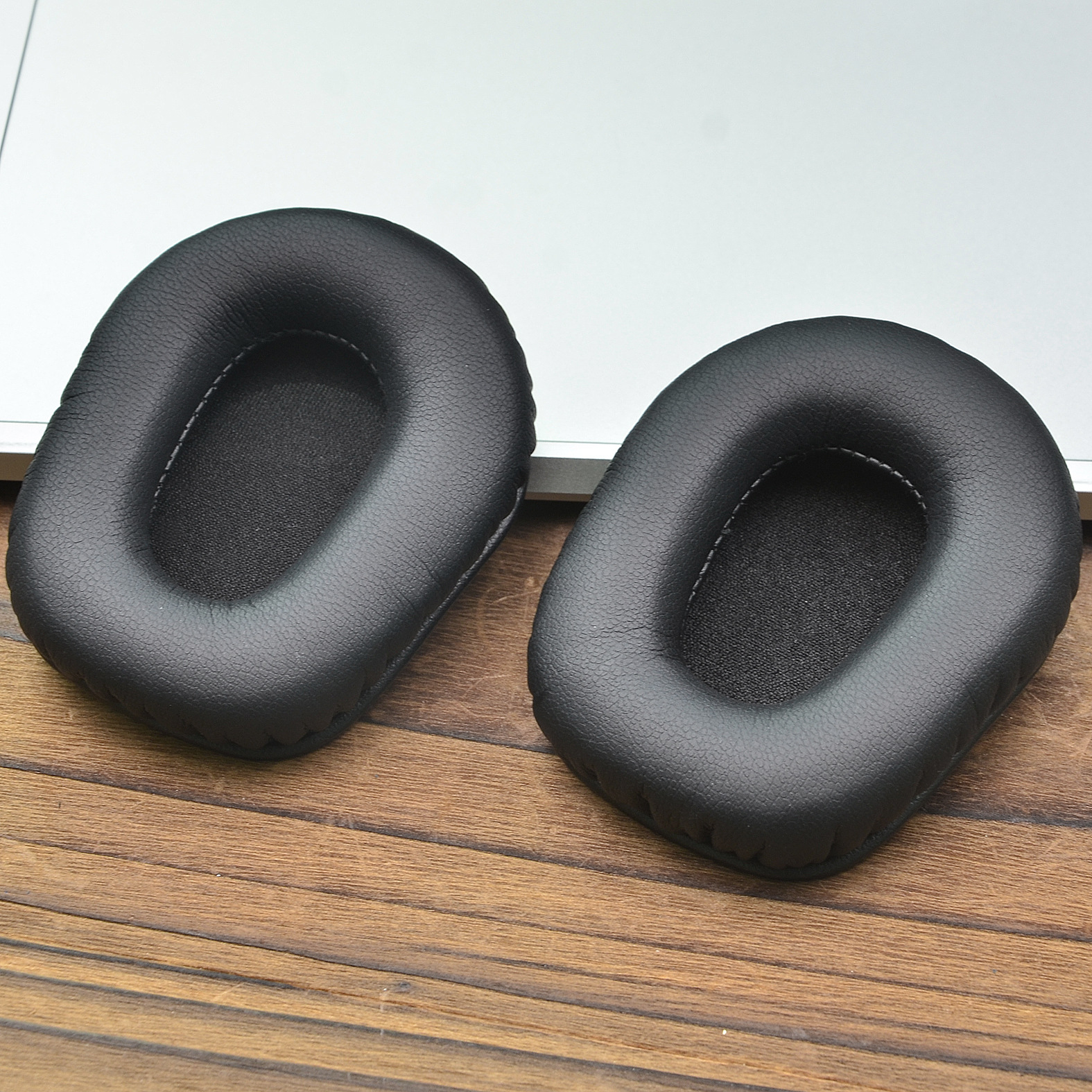 Due cuscinetti neri per le orecchie su una superficie di legno. I cuscinetti sono di forma ovale.