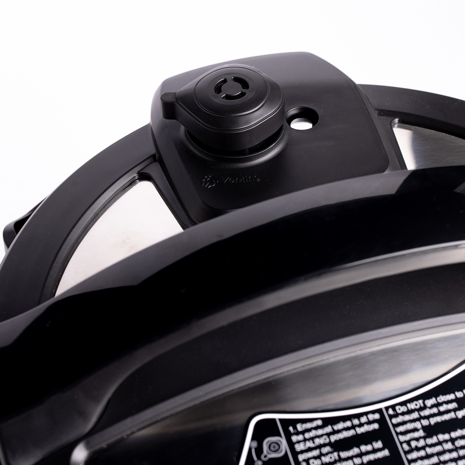 Black pressure cooker lid with a vent and safety instructions. Close-up view.