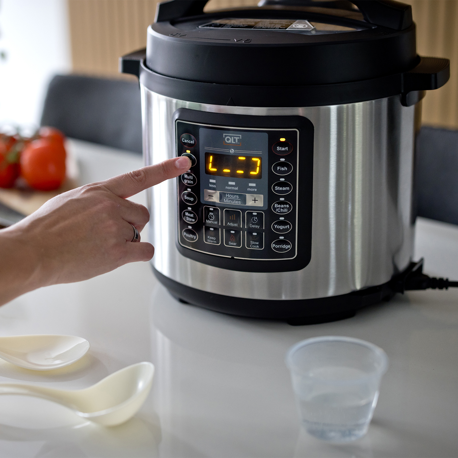 A person's hand presses a button on a silver and black pressure cooker. Other items are visible.