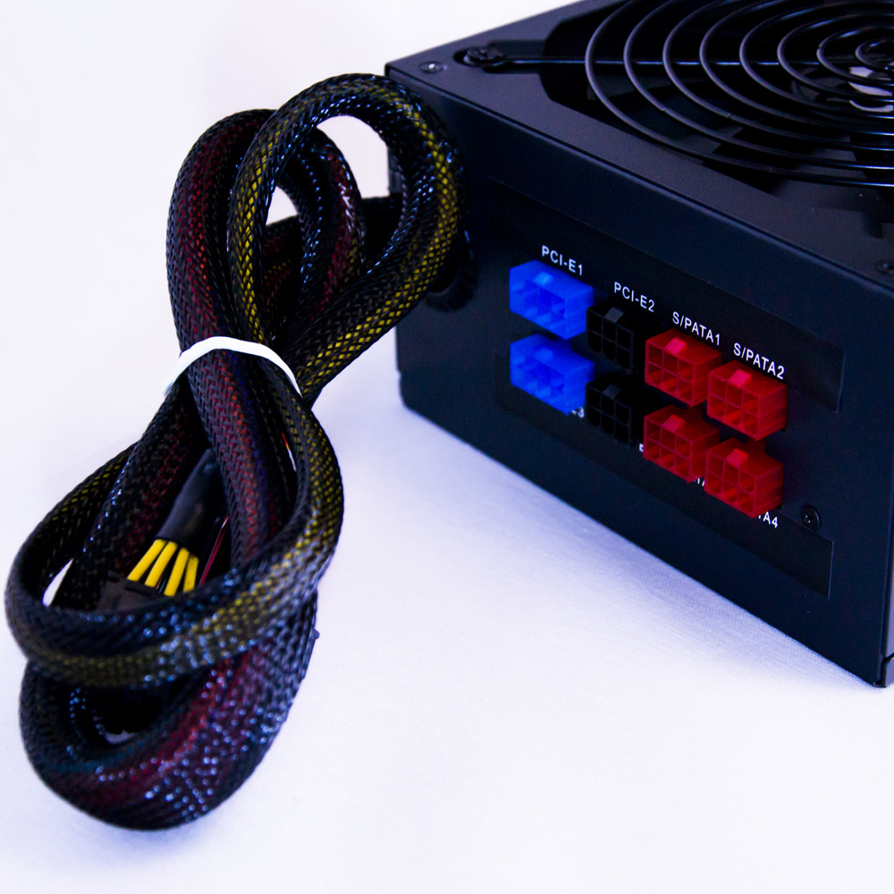 Primer plano de una fuente de alimentación negra con cables. Conectores azules y rojos visibles.