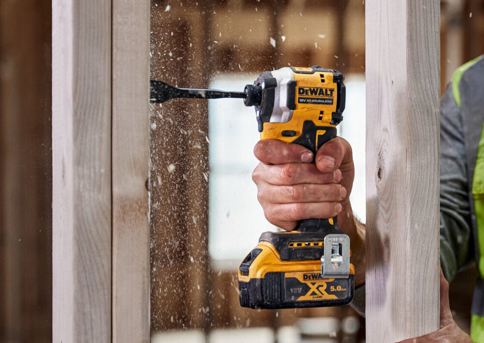 Osoba używająca żółtej wiertarki DeWalt na drewnie, z trocinami.
