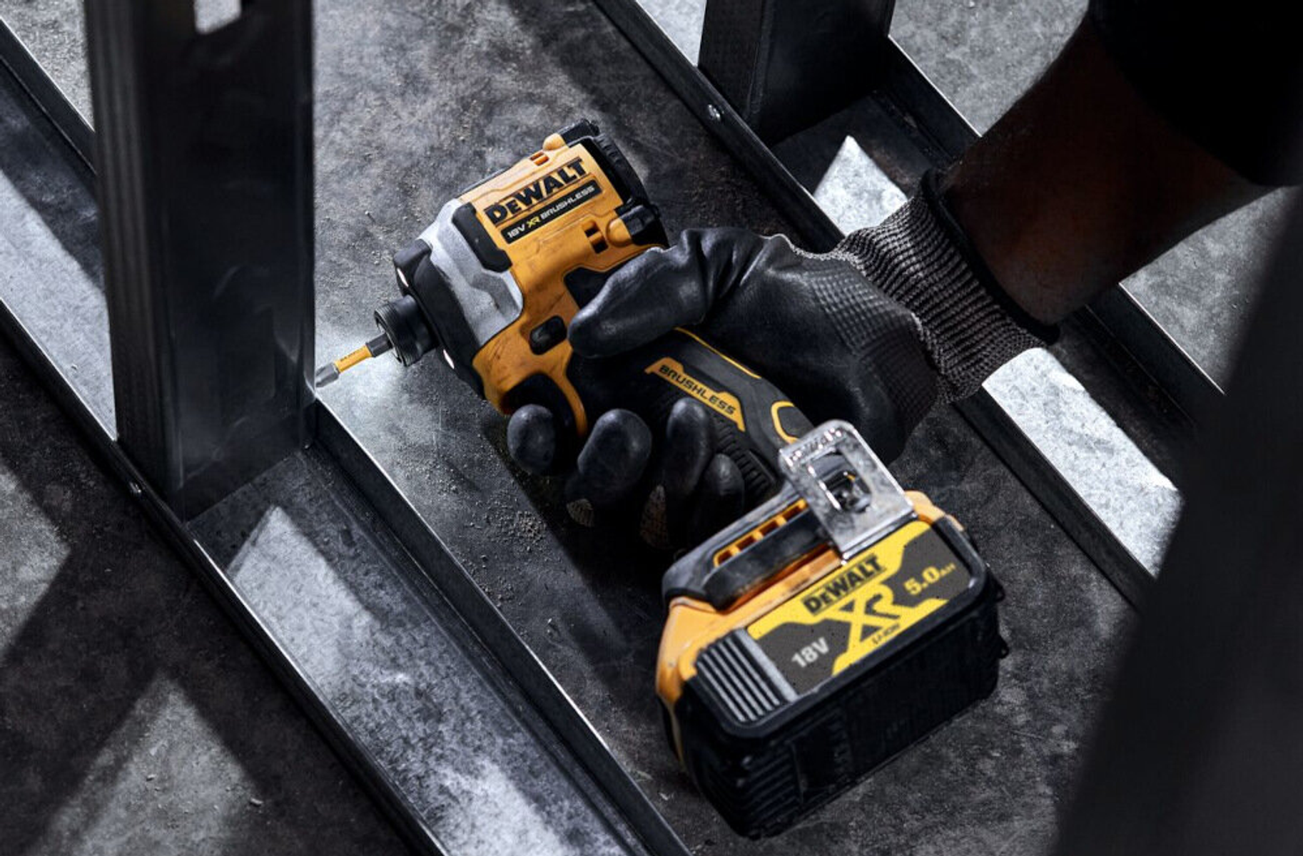 Żółto-czarna wiertarka DeWalt w użyciu. Tło z metalowej ramy.