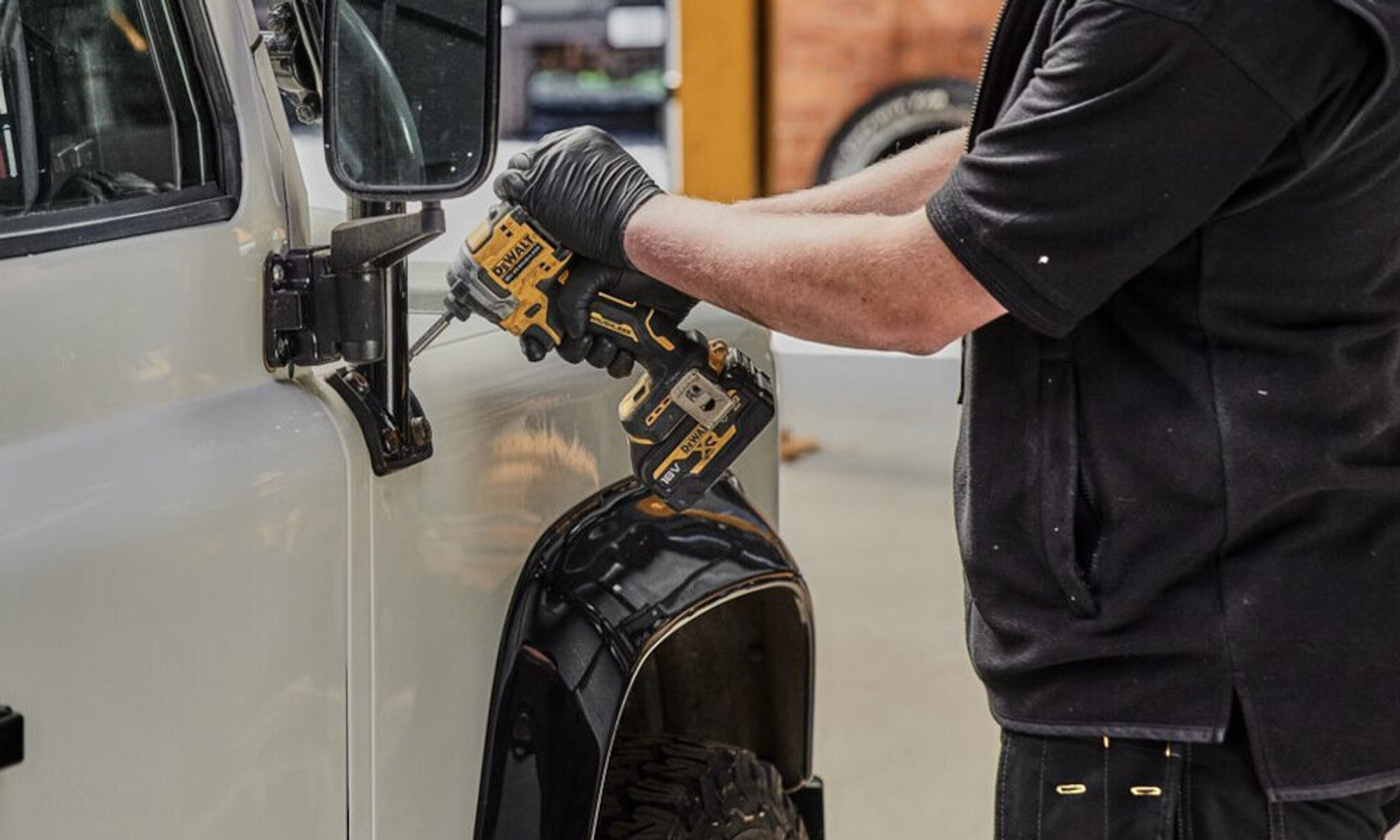 Osoba używająca wiertarki elektrycznej do zamocowania lusterka samochodowego do białego pojazdu.