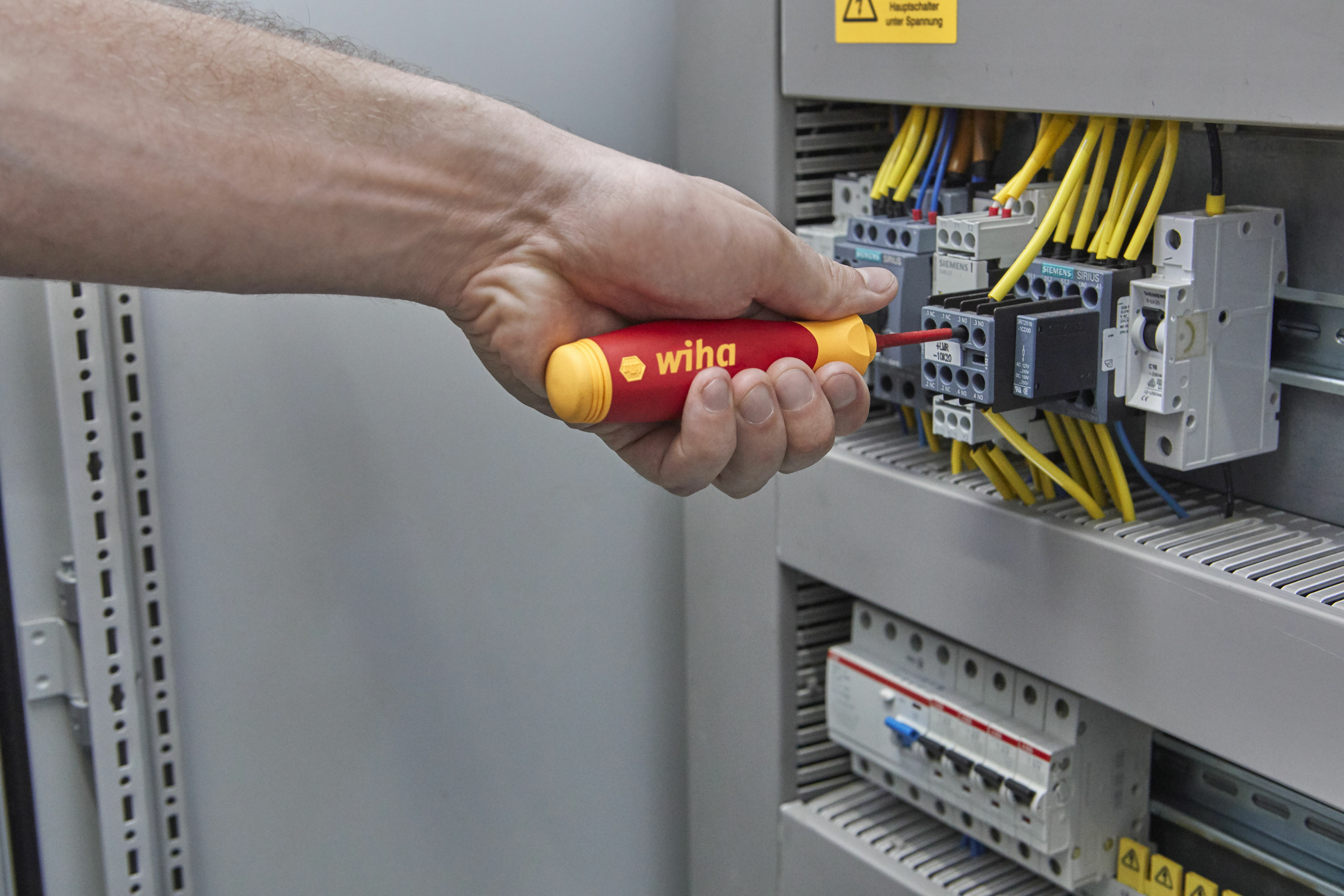 Dłoń używająca czerwono-żółtego śrubokrętu Wiha na panelu elektrycznym.