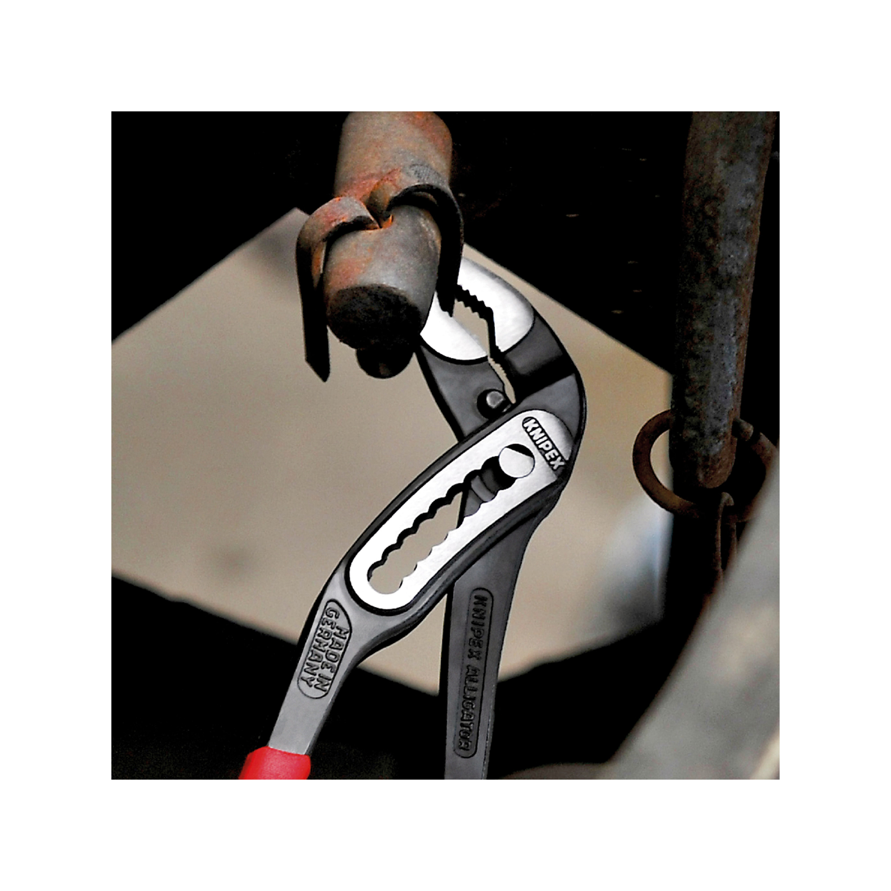 Szczypce Knipex chwytające metalową rurę, widoczne czerwone uchwyty.