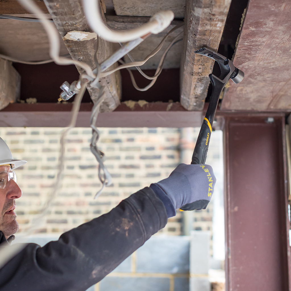 Osoba używająca młotka do usuwania drewna. Scena jest w pomieszczeniu.