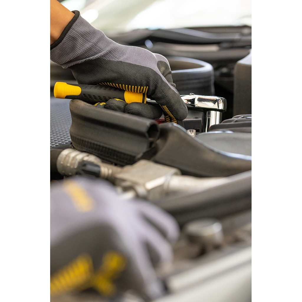 Eine Hand mit Handschuh benutzt einen Ratschenschlüssel an einem Automotor. Gelb-schwarzer Griff.