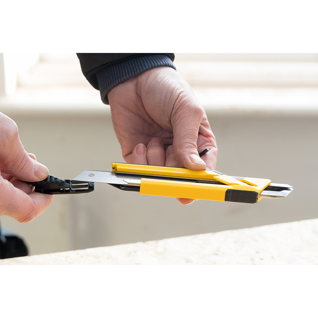 Eine Hand schneidet mit einem gelb-schwarzen Cuttermesser auf einer Holzoberfläche.