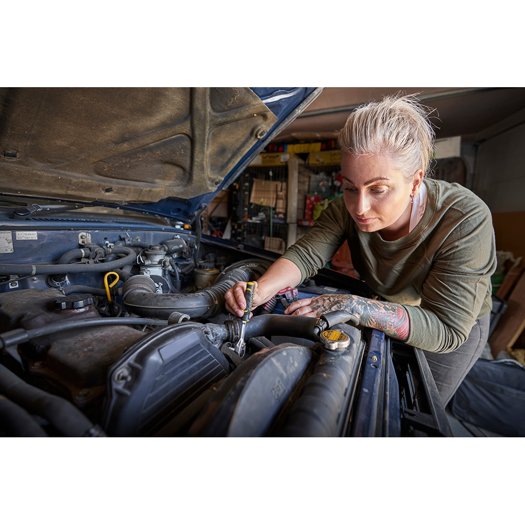 Eine Frau arbeitet an einem Automotor und verwendet einen Ratschenschlüssel.