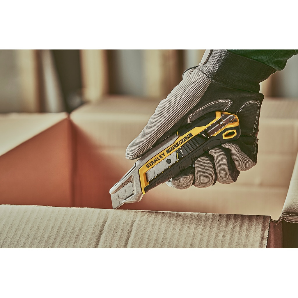 Behandschuhte Hand benutzt ein Universalmesser. Kartonhintergrund. Stanley FatMax Messer.