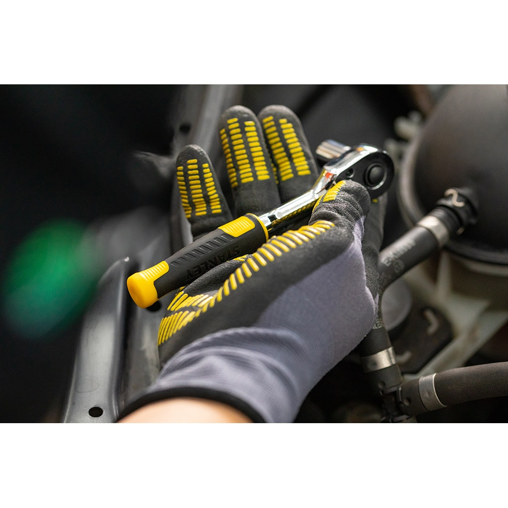 Eine Hand mit Handschuh hält einen Ratschenschlüssel mit schwarz-gelbem Griff in der Nähe eines Autos.