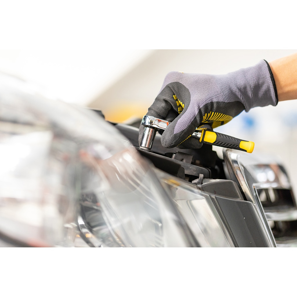 Eine Person, die einen Ratschenschlüssel benutzt, um an einem Auto zu arbeiten. Der Schraubenschlüssel hat einen gelb-schwarzen Griff.