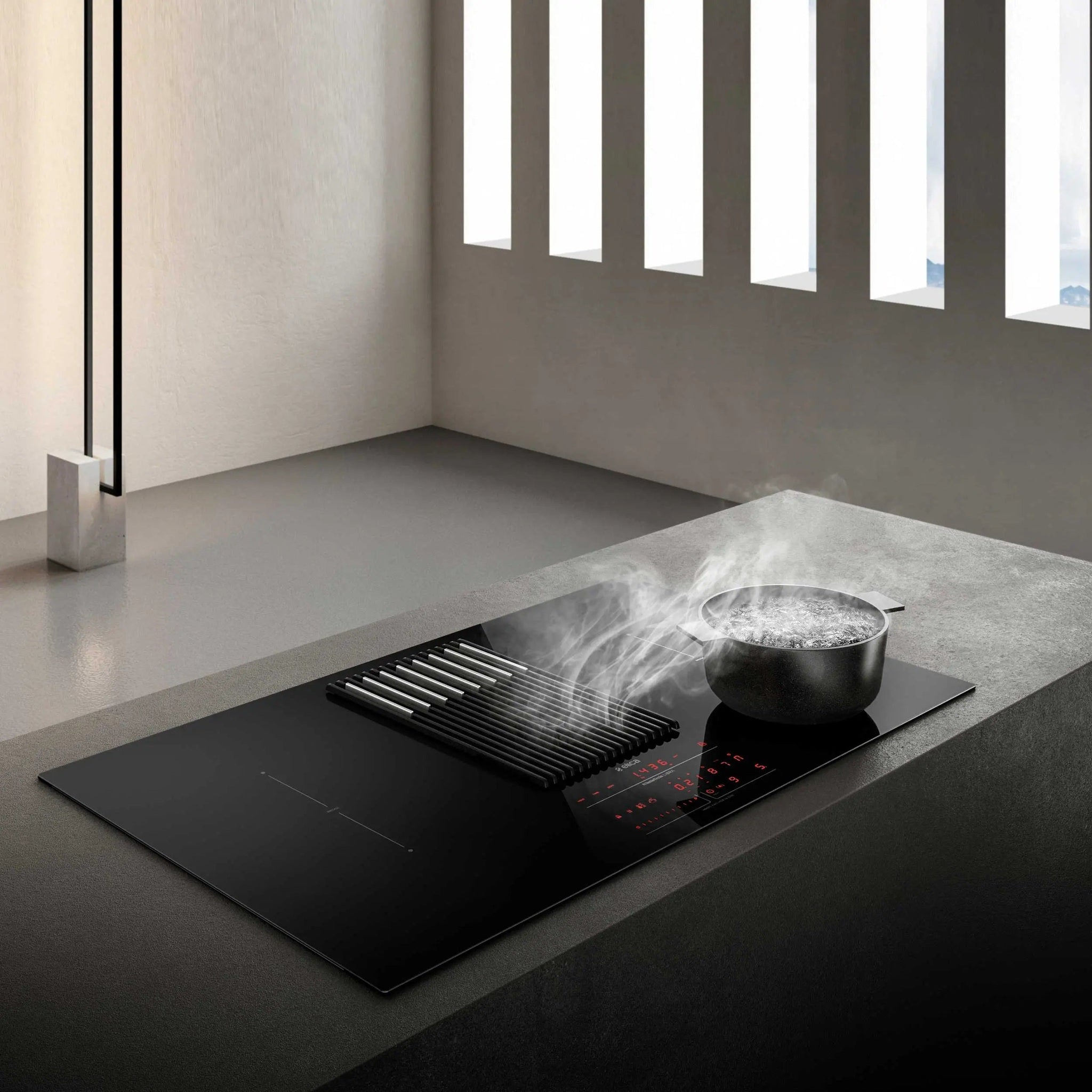 Placa de cocina negra con ventilación integrada, olla con agua hirviendo y ventana al fondo.