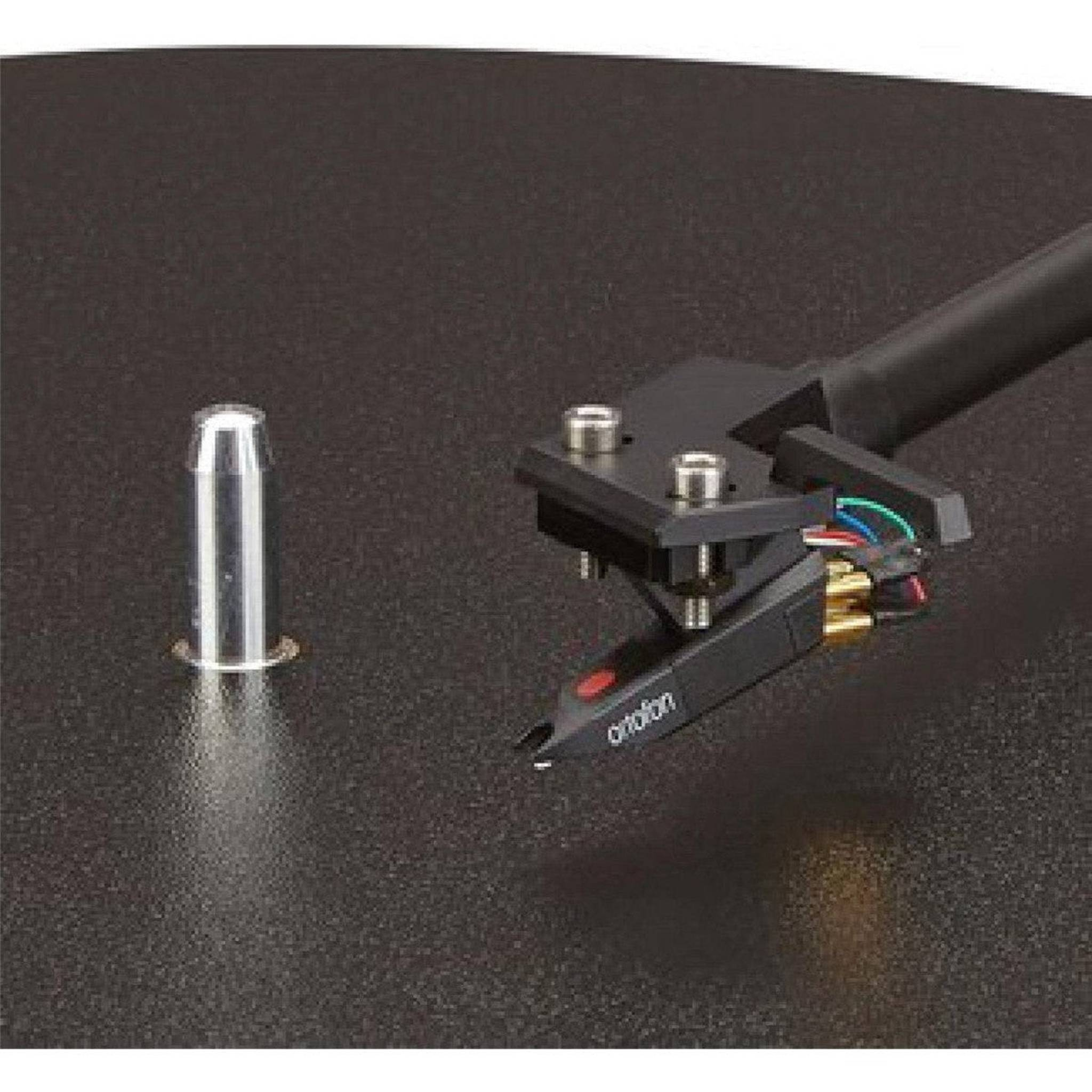 Igła gramofonowa i wkładka, obok osłona igły na ciemnej powierzchni.