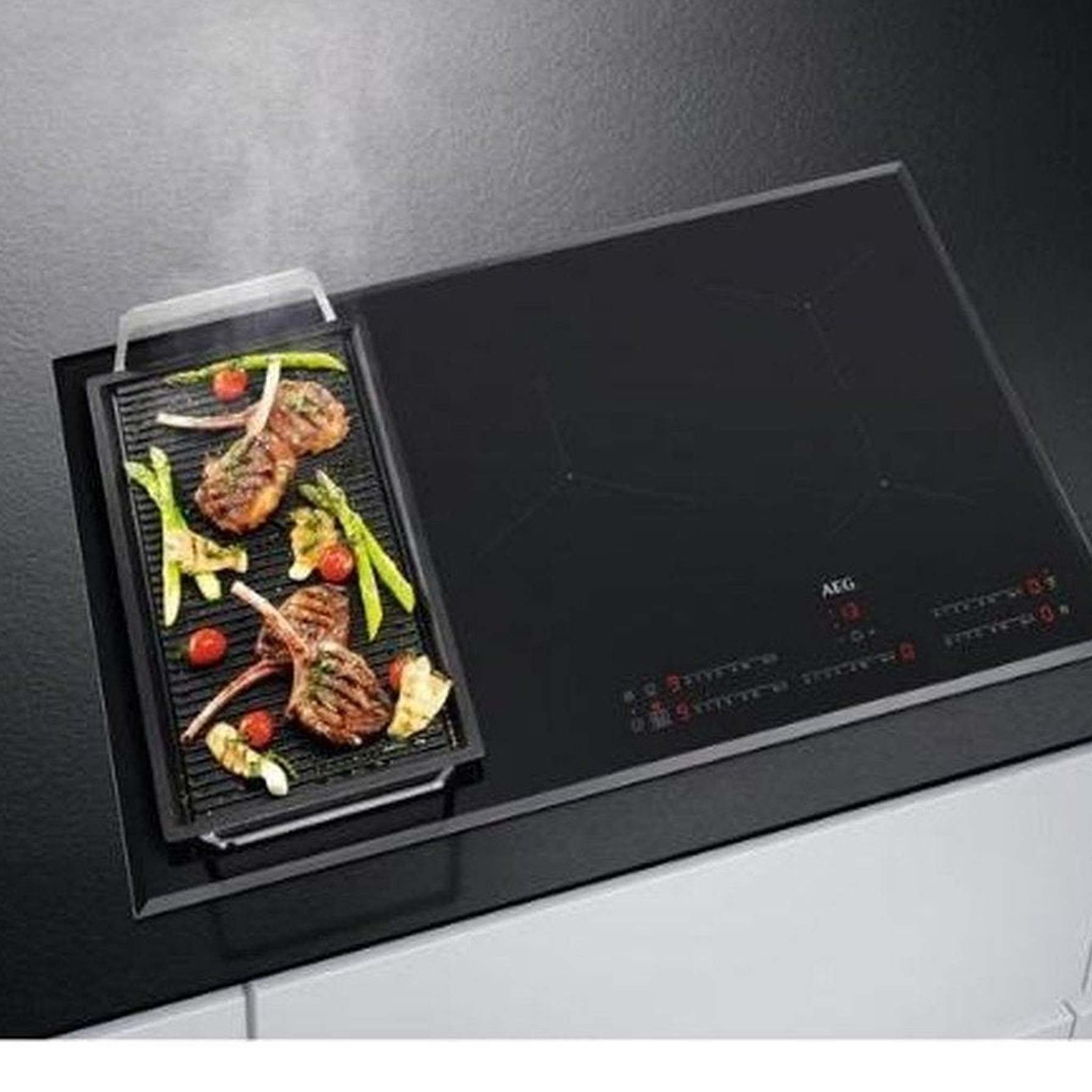 Een inductiekookplaat met een grillpan met gekookt vlees en groenten erop.