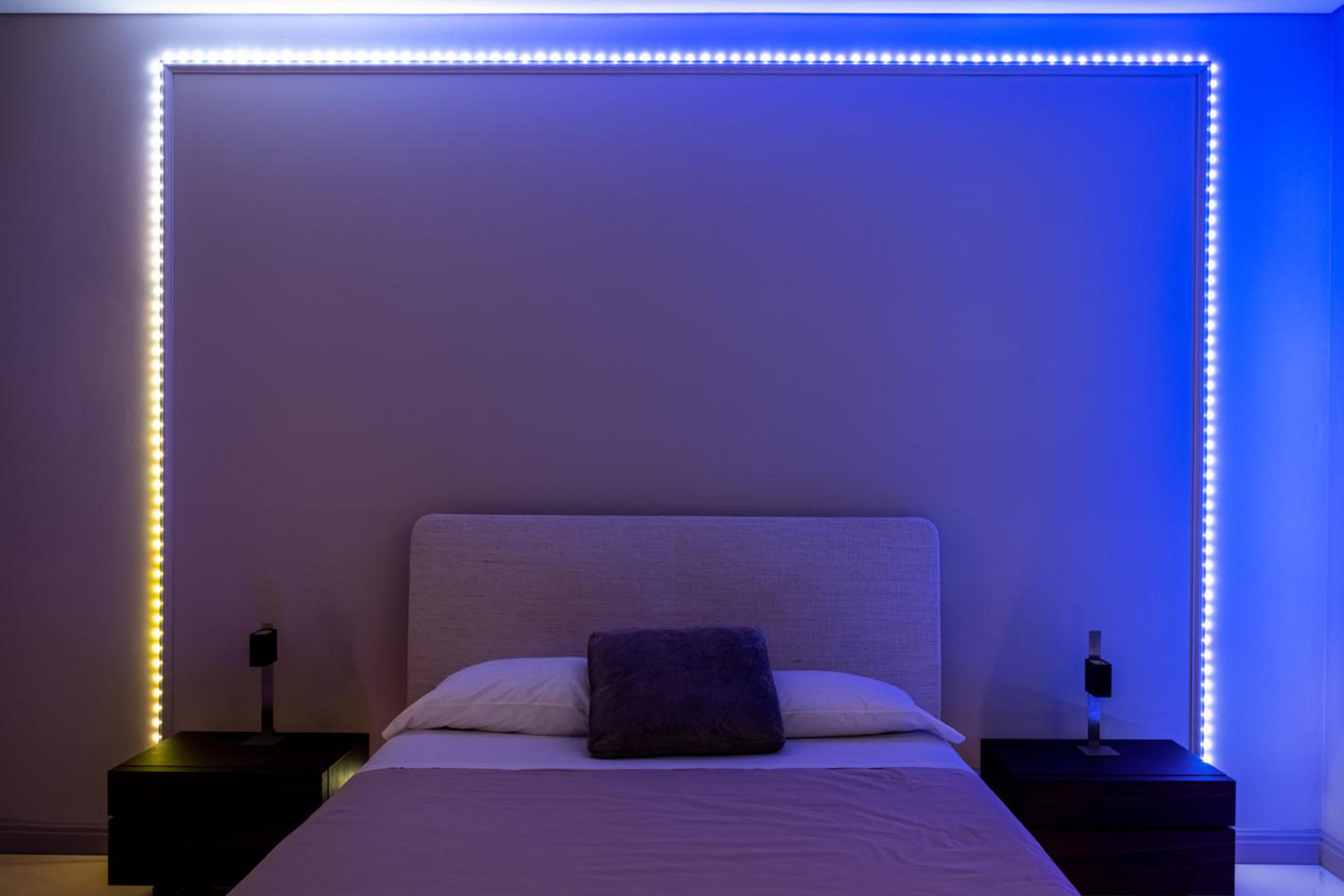 Sypialnia z łóżkiem i światłami. Światła to paski LED wokół ściany. To ciemny pokój.