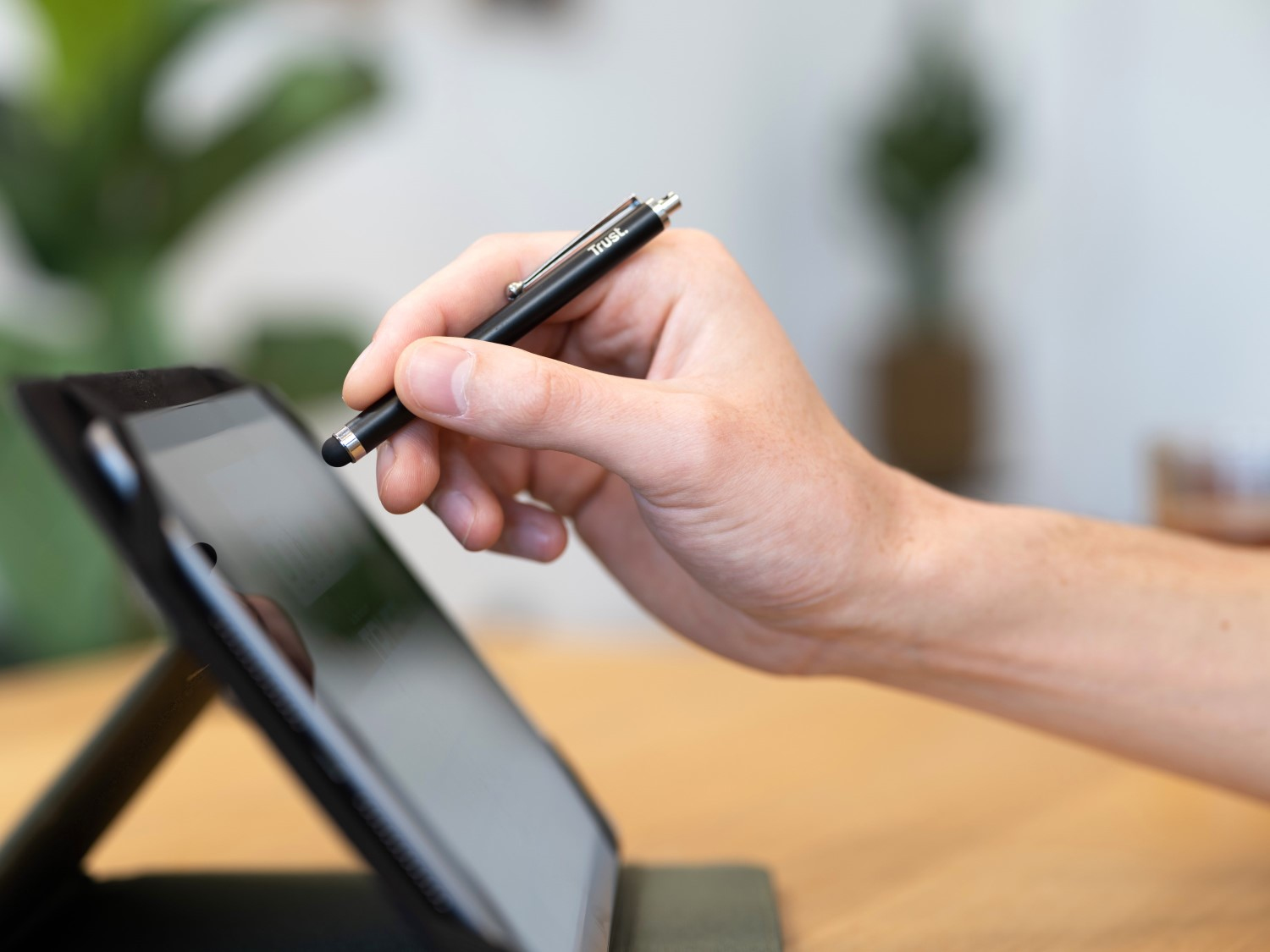 Ręka trzymająca czarny rysik, pisząca na tablecie na drewnianym stole.