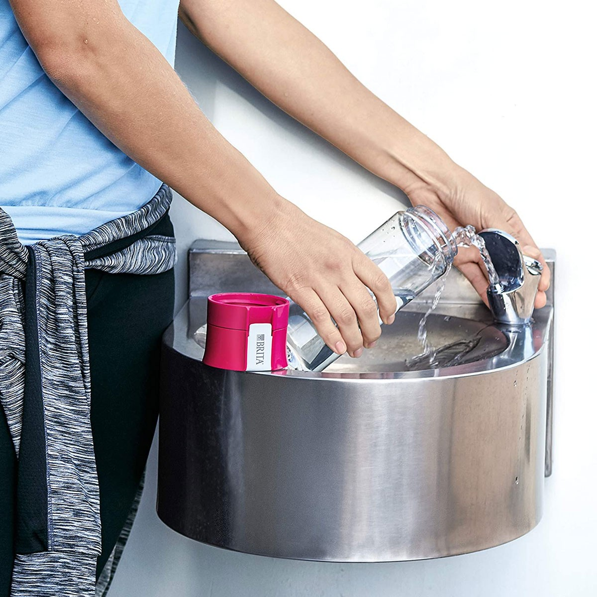 Persona che riempie una bottiglia d'acqua trasparente a una fontana. Bottiglia rosa di lato.