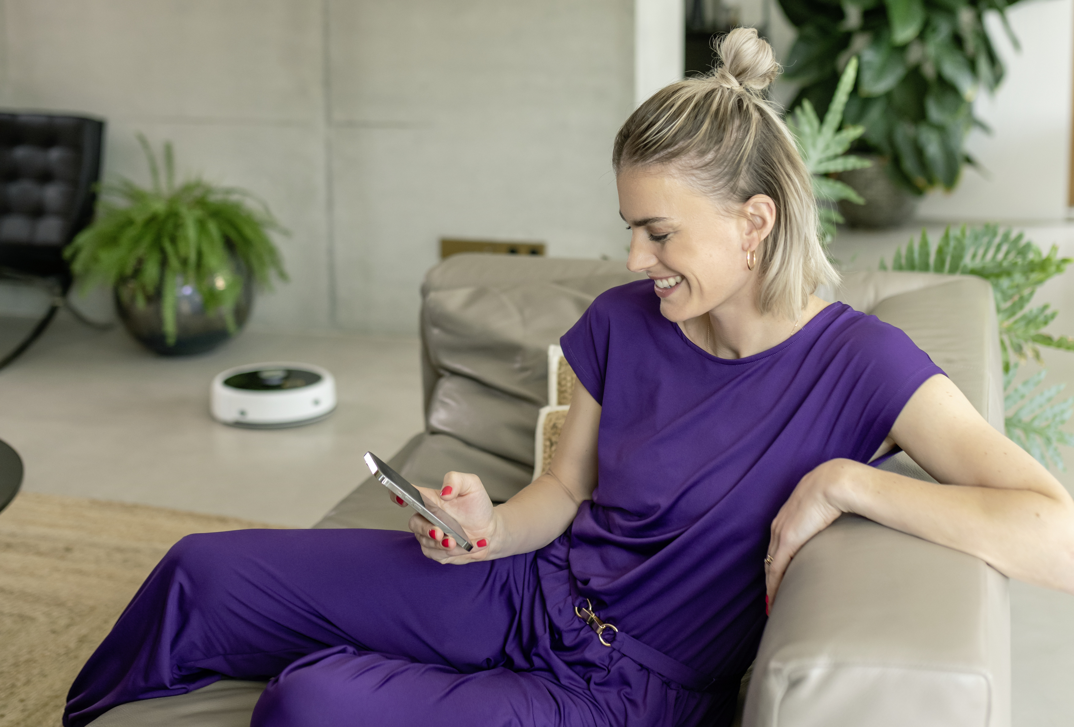 Kobieta w fiolecie korzystająca z telefonu siedząc na sofie.