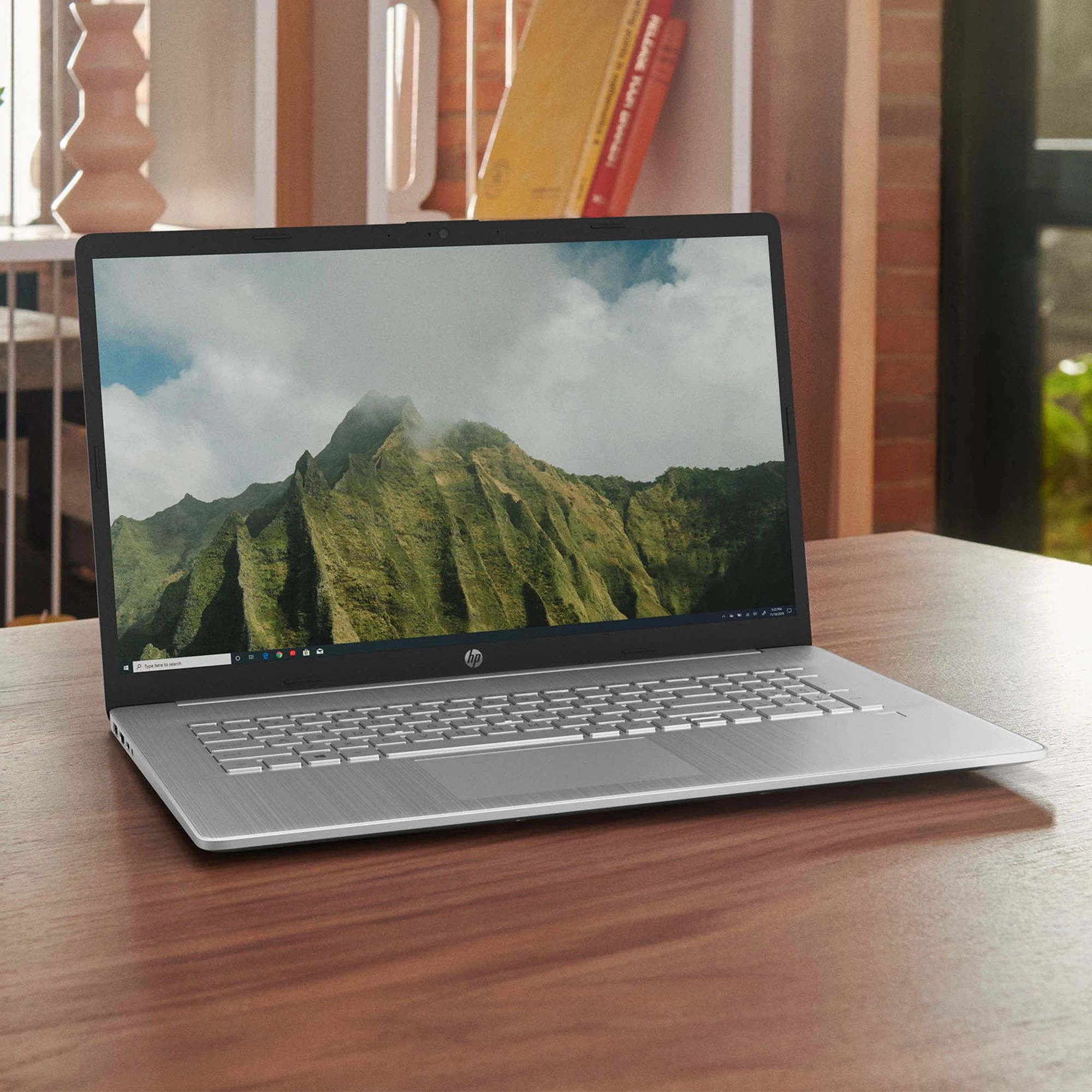 Ein silberner Laptop auf einem Holztisch, geöffnet mit einem Bildschirm, der eine Berglandschaft zeigt, in einem Raum.