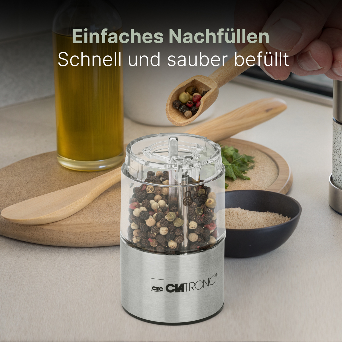 Młynek do pieprzu z pieprzem, drewnianą łyżką, butelką oleju i miską na stole.