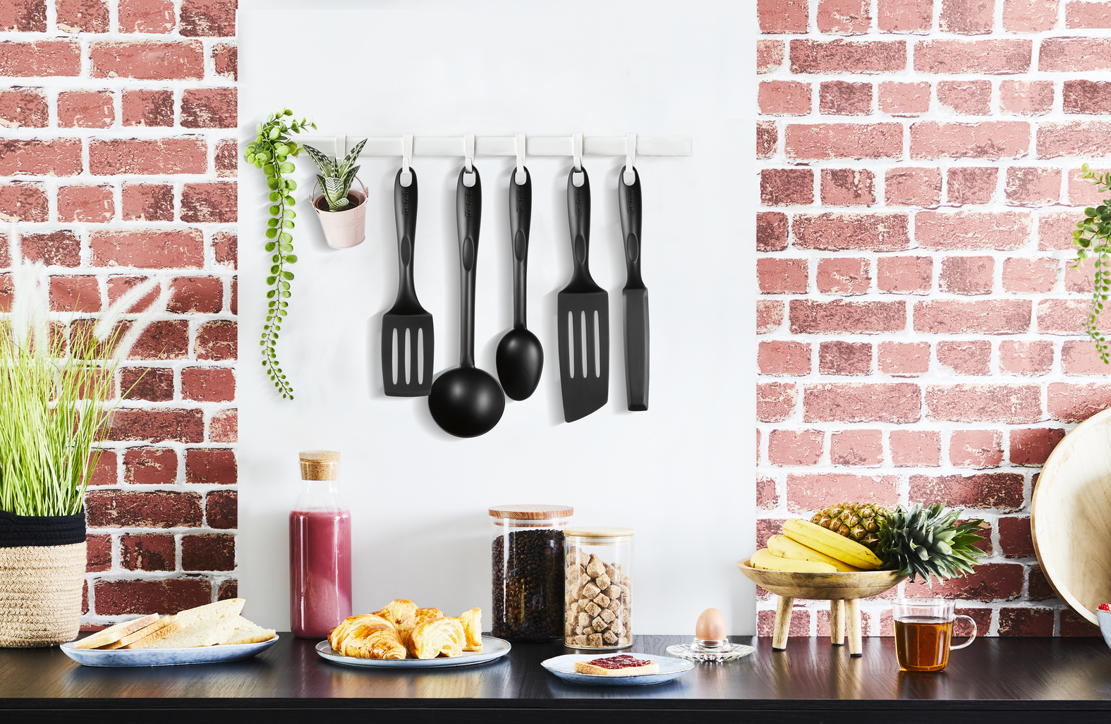 Küchenszene: Utensilien hängen an der Wand, Essen auf der Theke. Ziegelmauer im Hintergrund.
