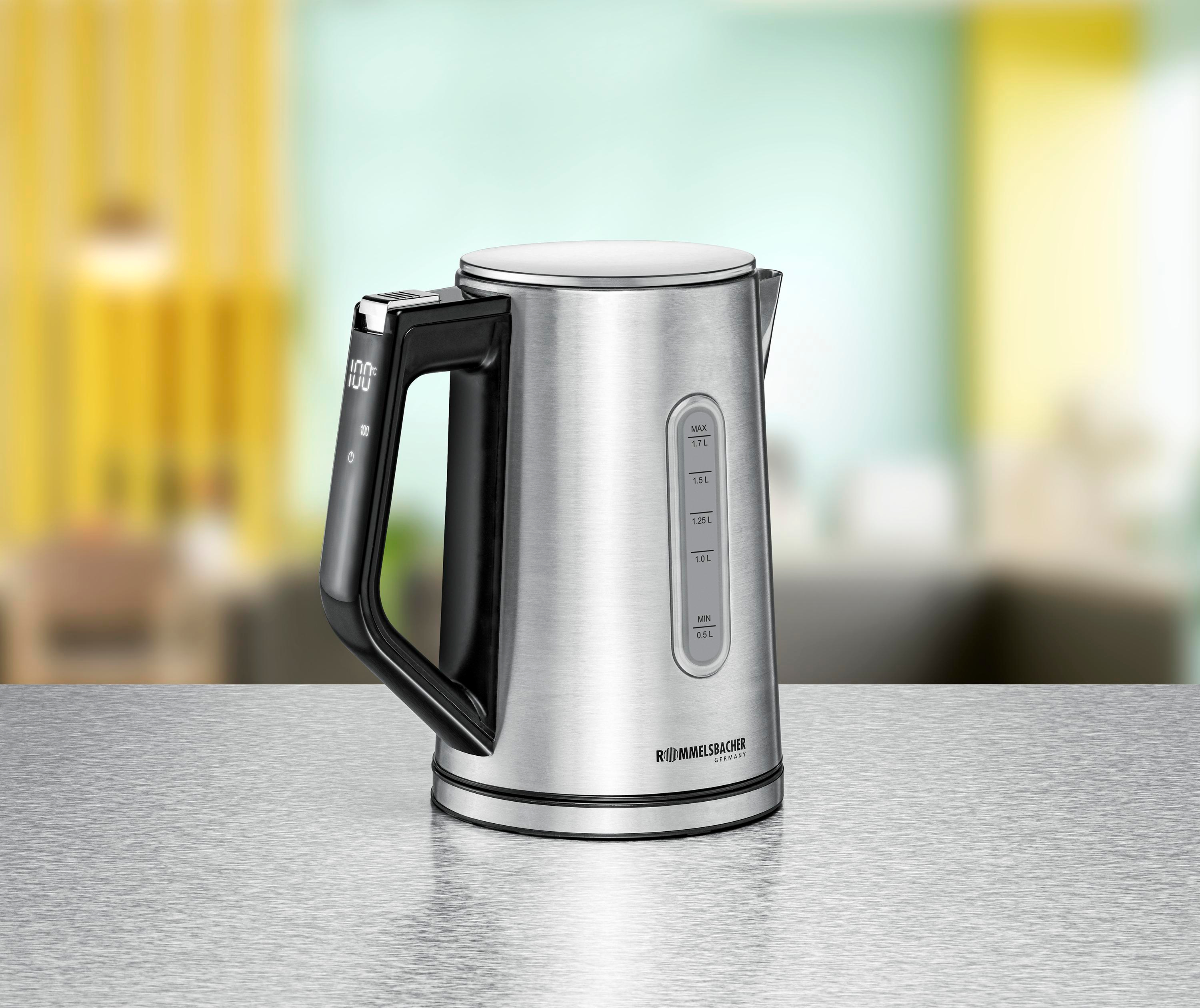 Srebrny czajnik na stole. Czarny uchwyt z wyświetlaczem. Tło: kuchnia.