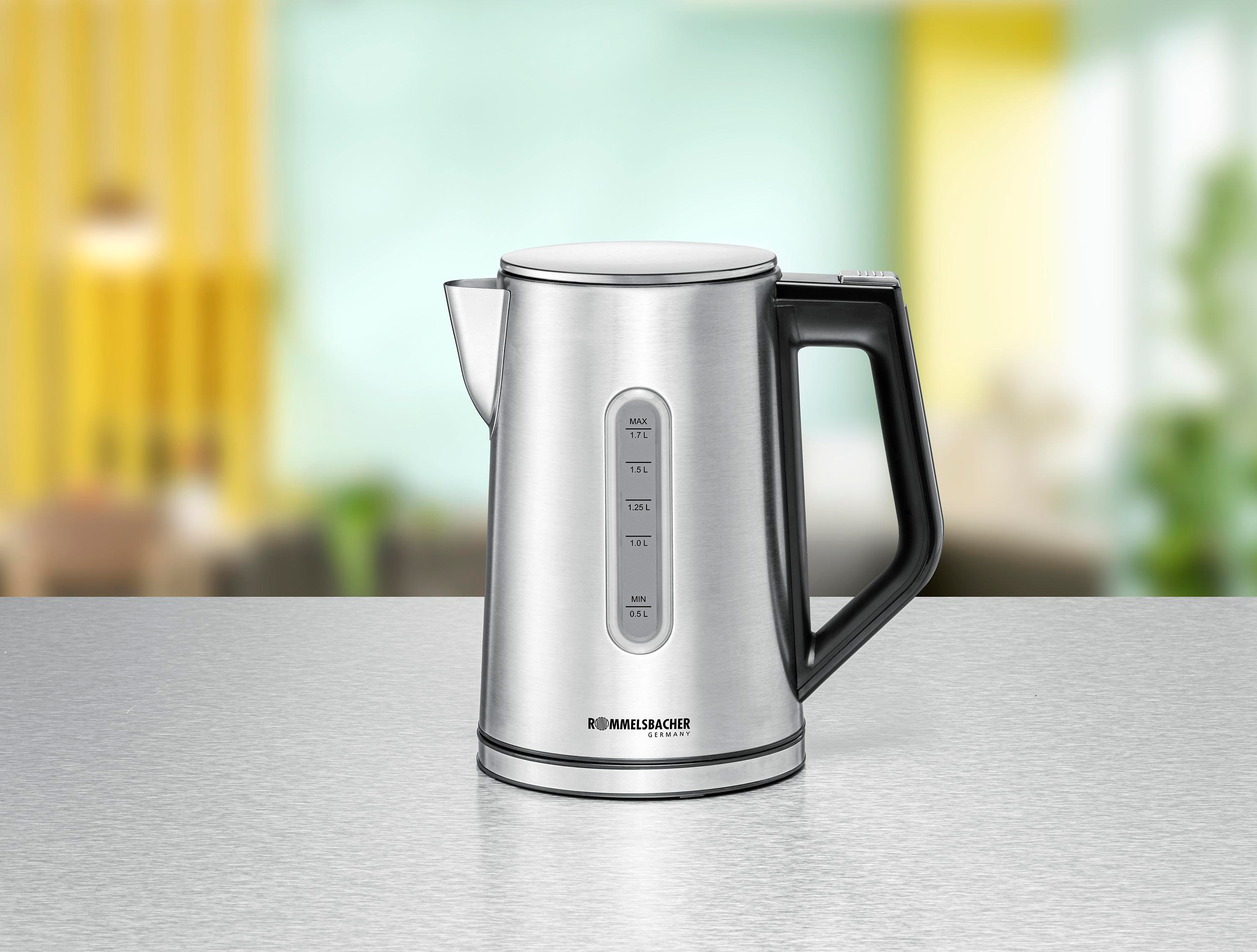 Czajnik elektryczny ze stali nierdzewnej na stole. Tło jest rozmyte, z żółtą zasłoną.