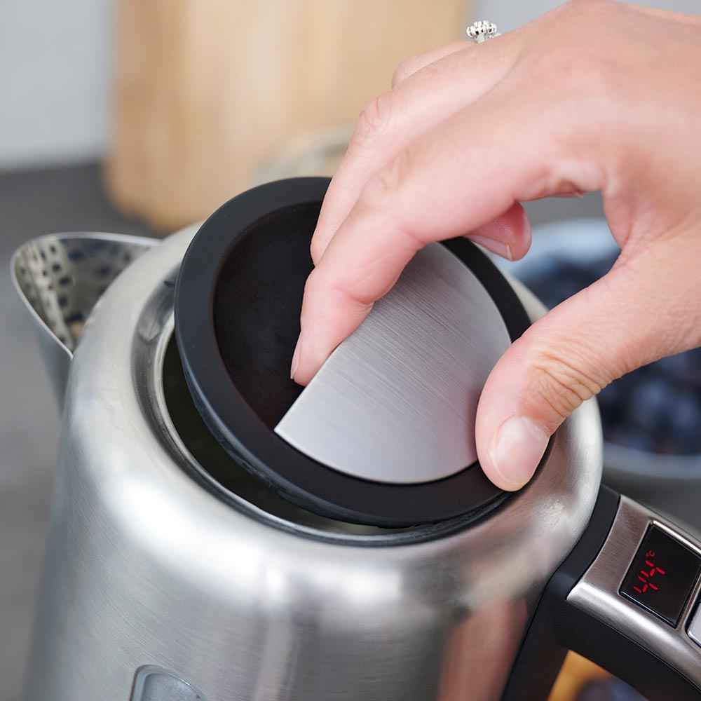 Ręka otwiera pokrywę czajnika. Czajnik jest ze stali nierdzewnej. Wyświetlacz cyfrowy pokazuje 44 stopnie.