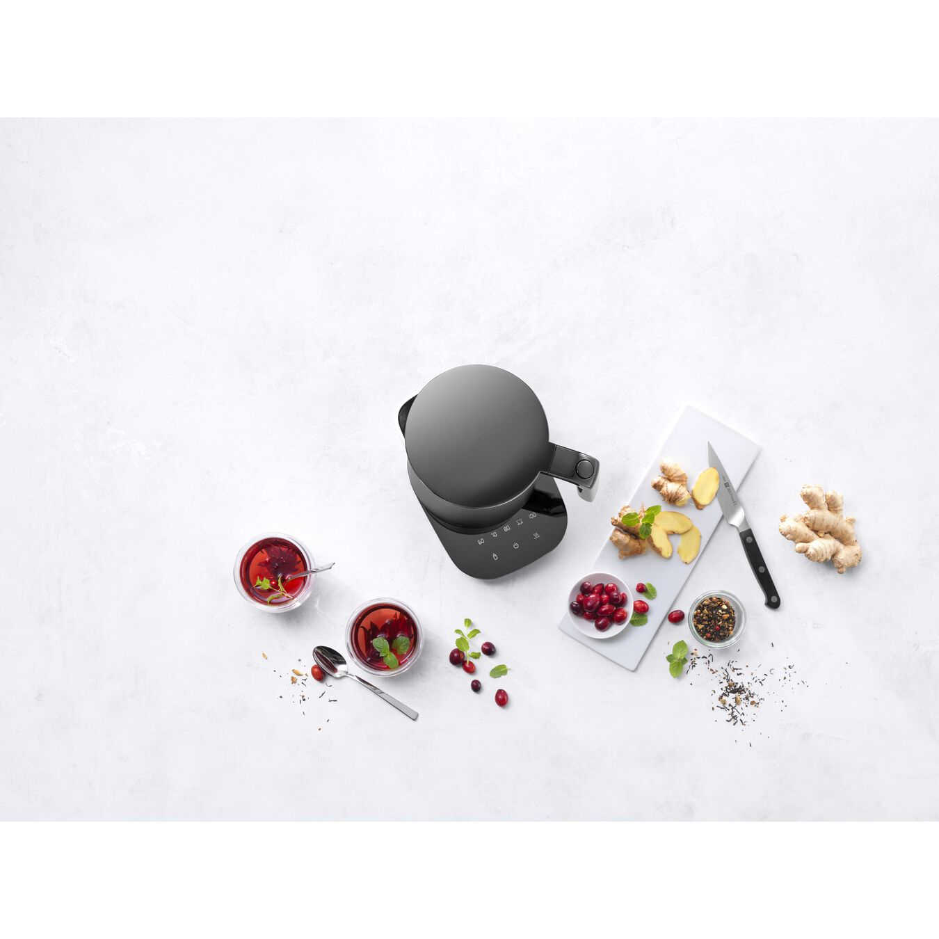 Czarny ekspres do herbaty z filiżankami, składnikami i białą deską do krojenia.