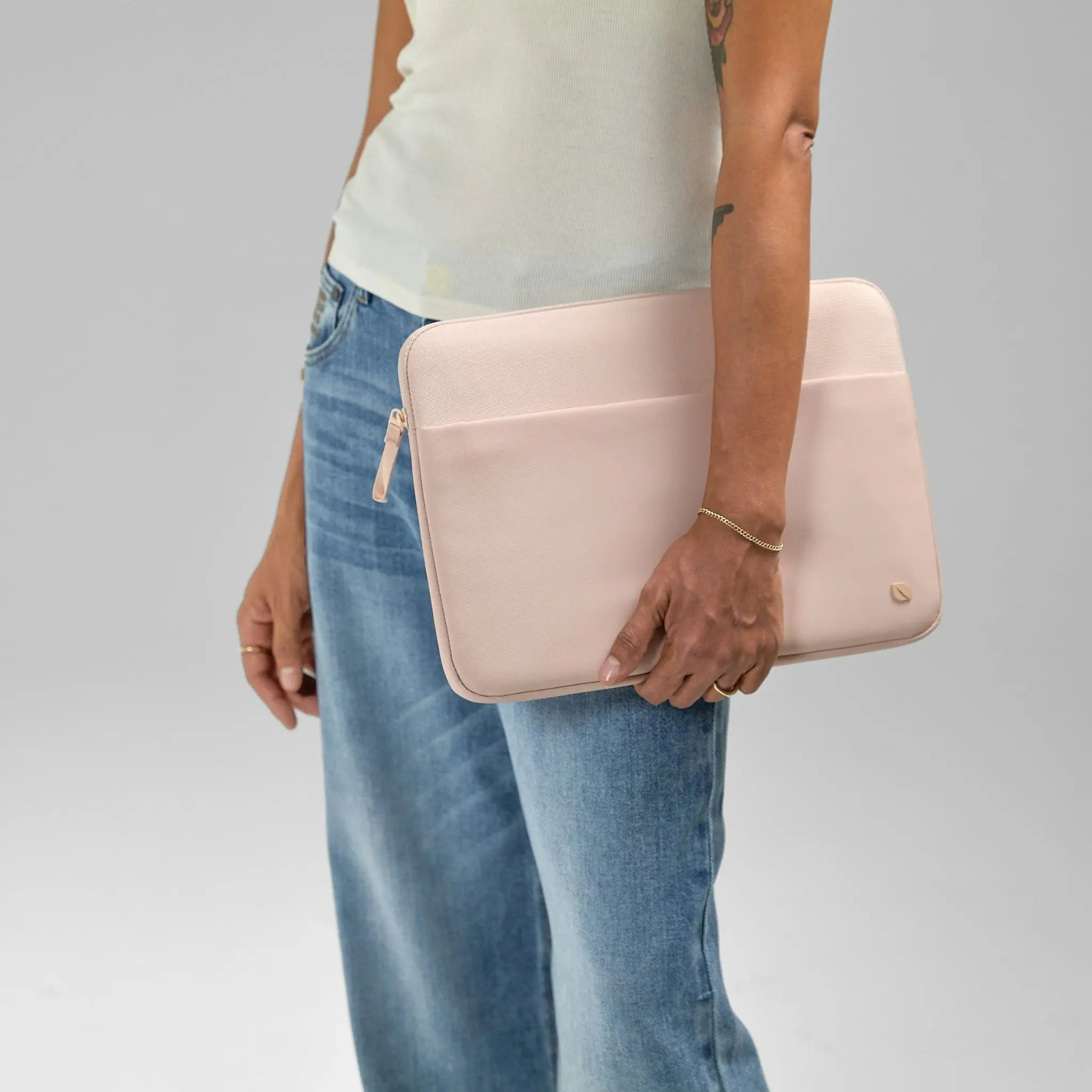 Una persona con jeans y una camiseta blanca sostiene una funda rosa para portátil.