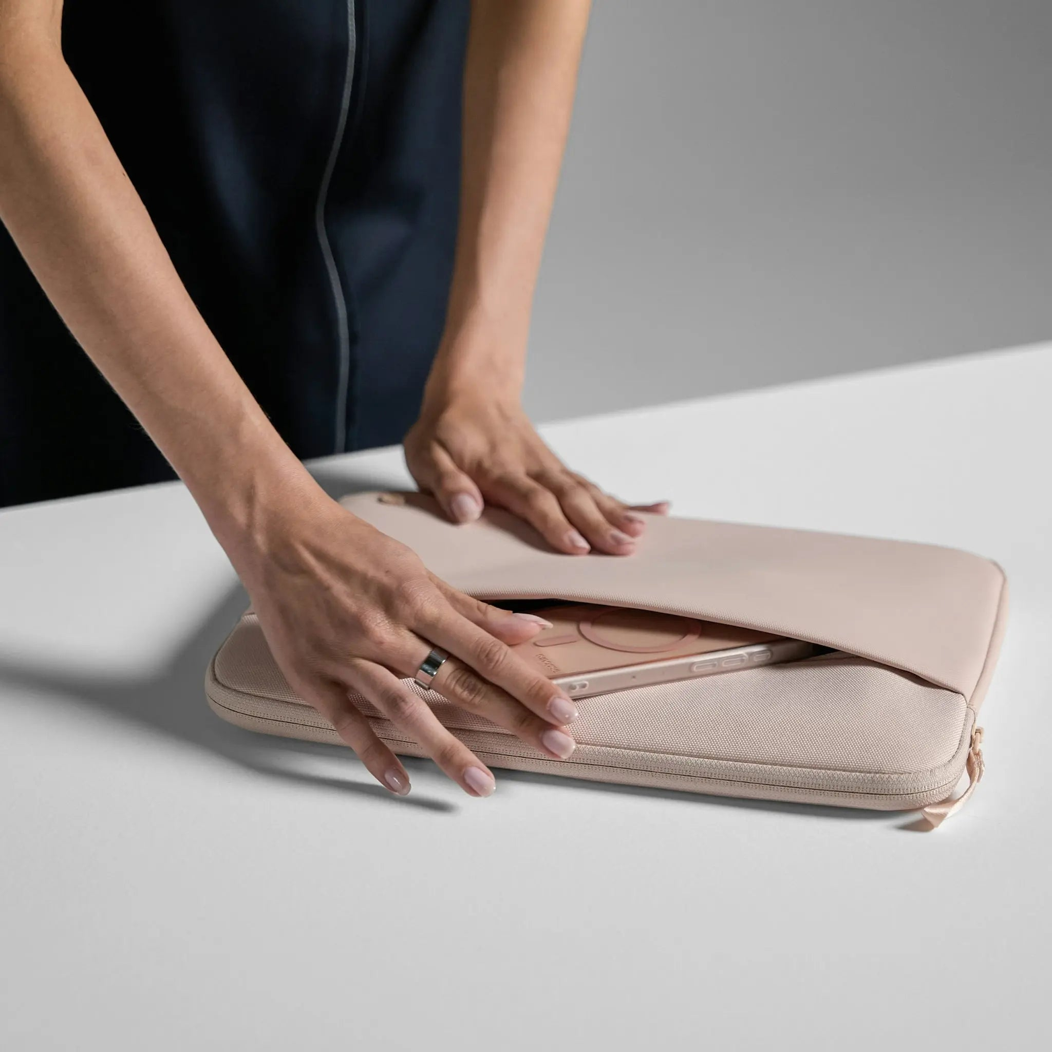 Manos sosteniendo funda rosa claro para portátil con teléfono parcialmente visible dentro.