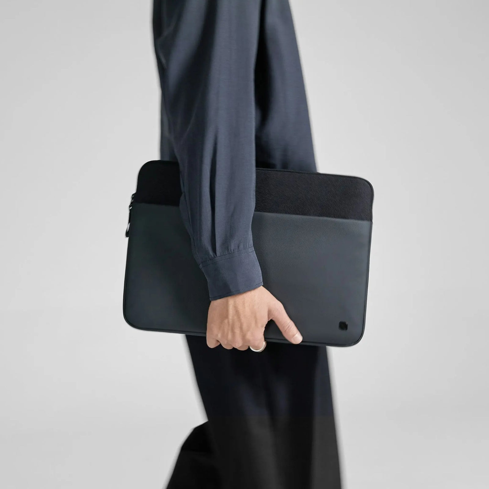 Una persona che tiene una custodia nera per laptop con la parte superiore nera e la parte inferiore grigia.