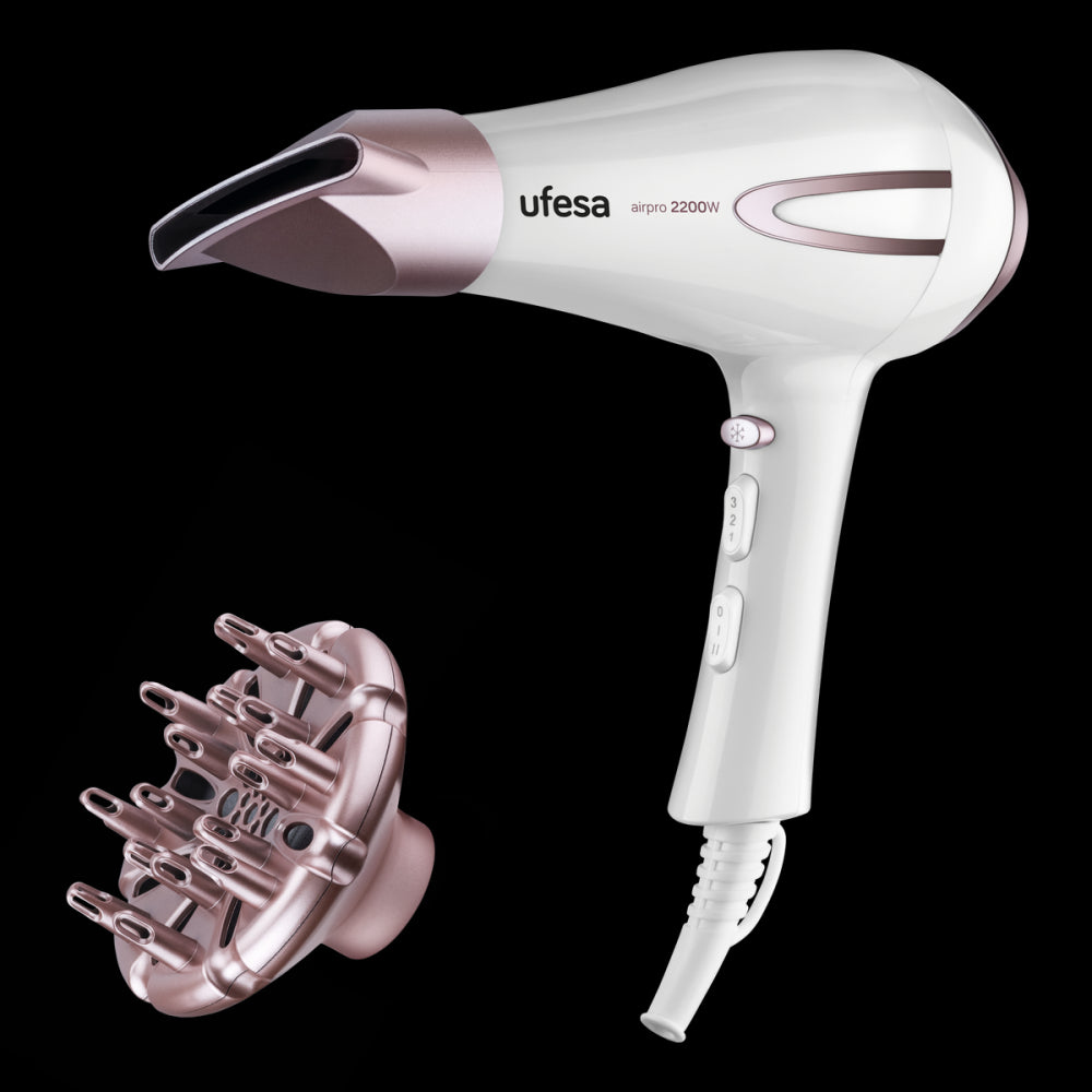 Biała suszarka do włosów, różowo-złote akcenty. Dysza obok na czarnym tle.