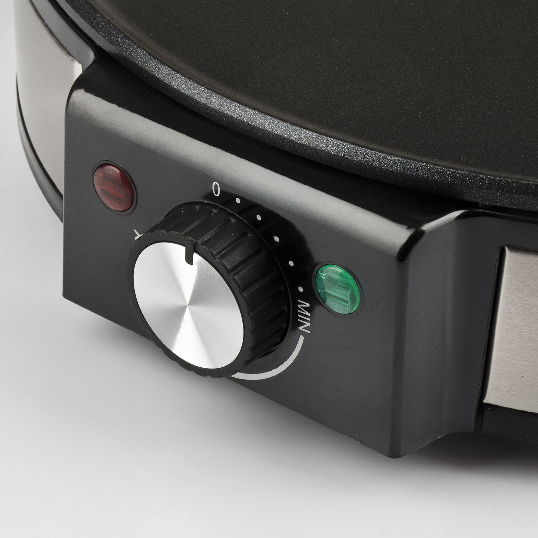 Zbliżenie czarnego panelu sterowania płyty grillowej, z pokrętłem i kontrolkami na białej powierzchni.