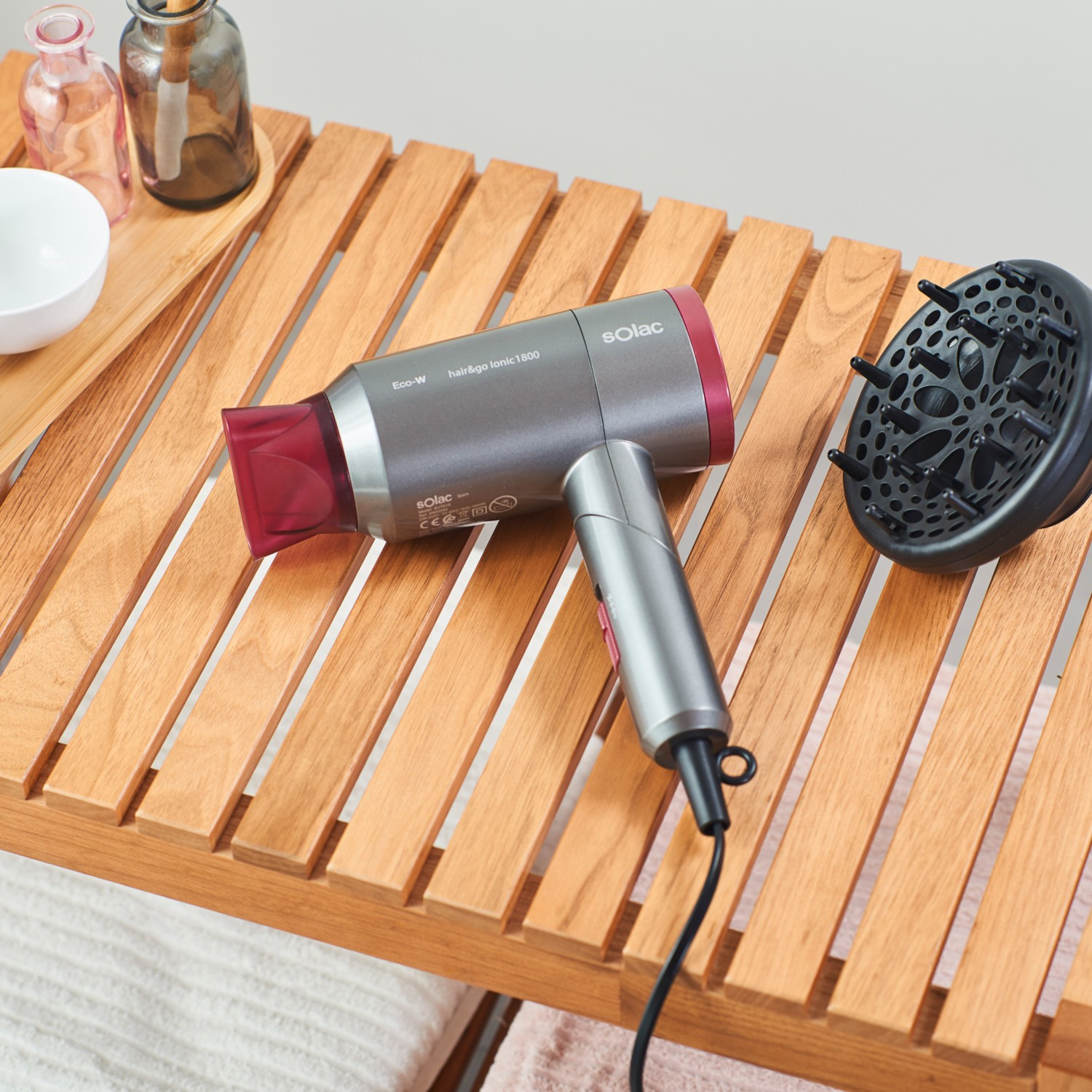 Suszarka do włosów i dyfuzor na drewnianym stojaku. Butelki w tle.