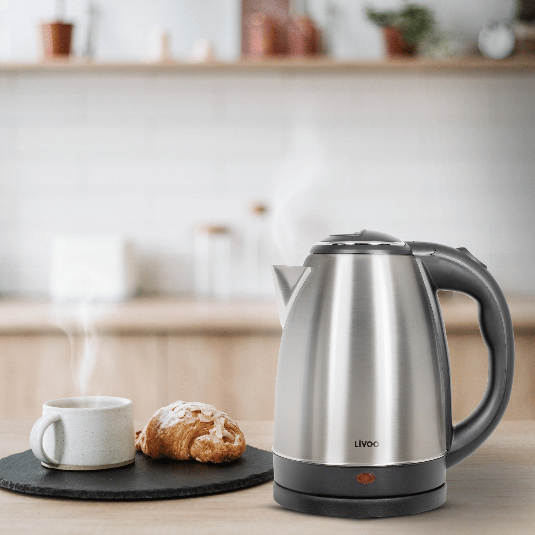 Bollitore elettrico in acciaio inossidabile con una tazza di caffè, un croissant e un tavolo di legno.