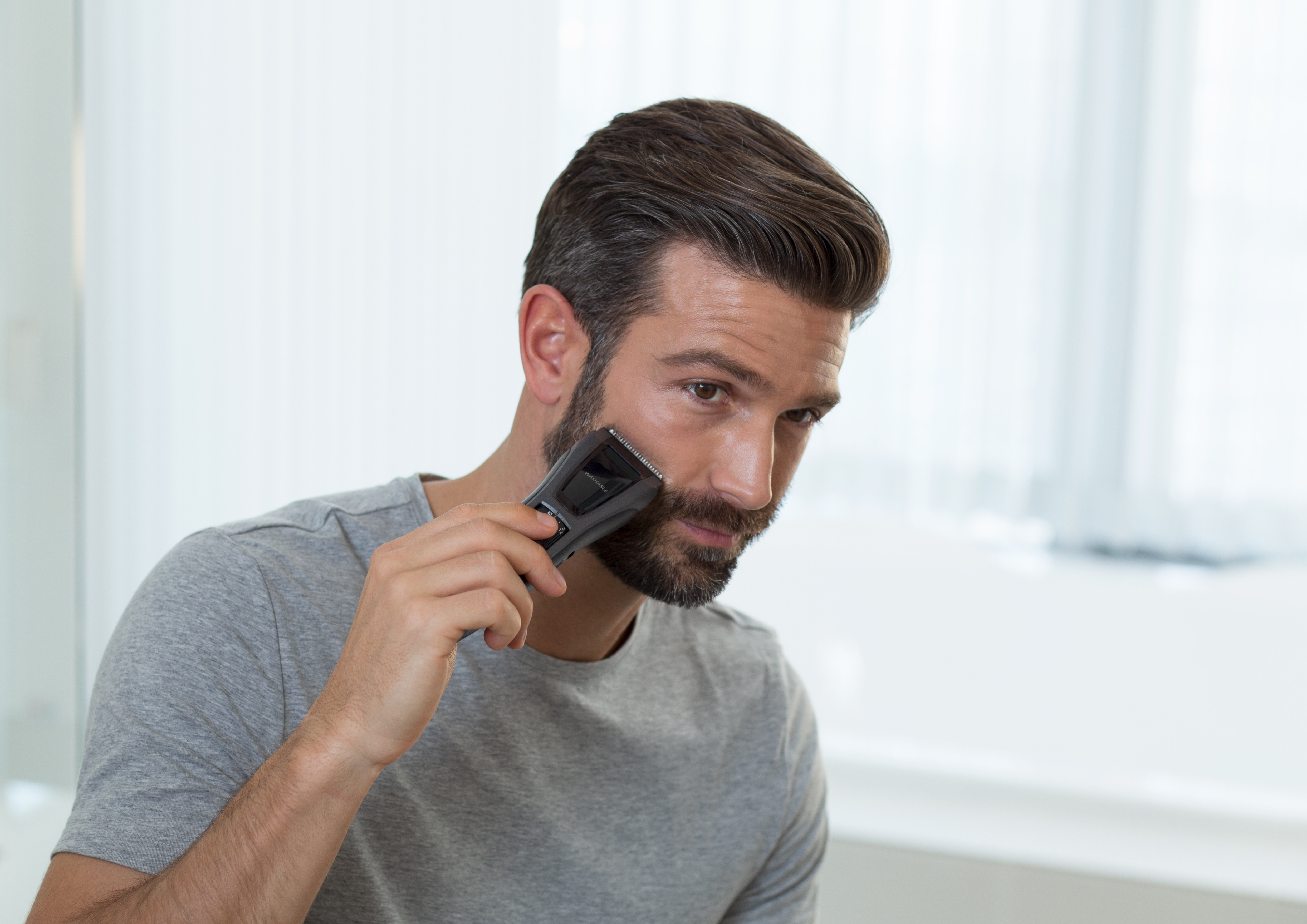 Mężczyzna goli brodę czarną maszynką, skupiając się na twarzy.