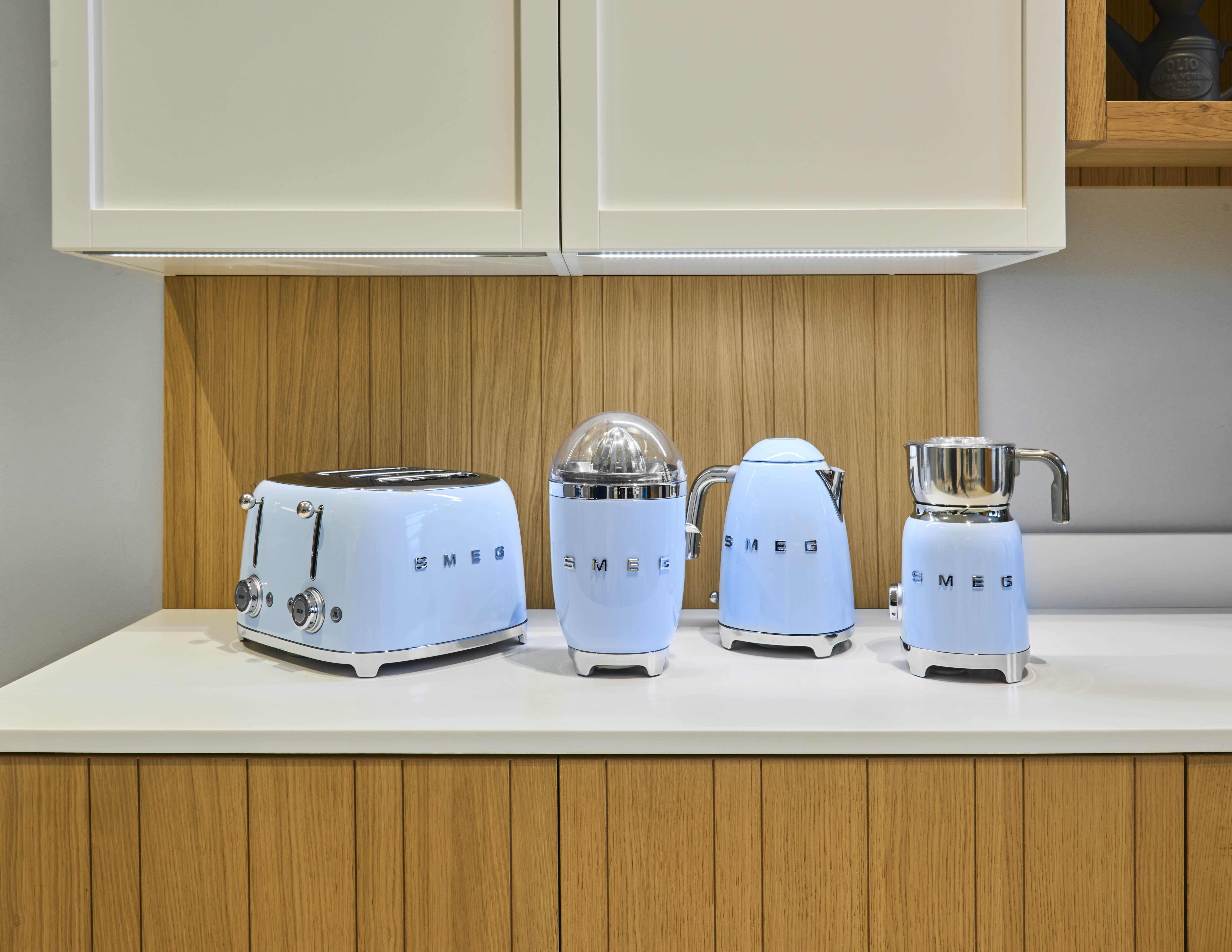 Vier hellblaue Küchengeräte auf einer Theke: Toaster, Entsafter, Wasserkocher und Kaffeemühle.