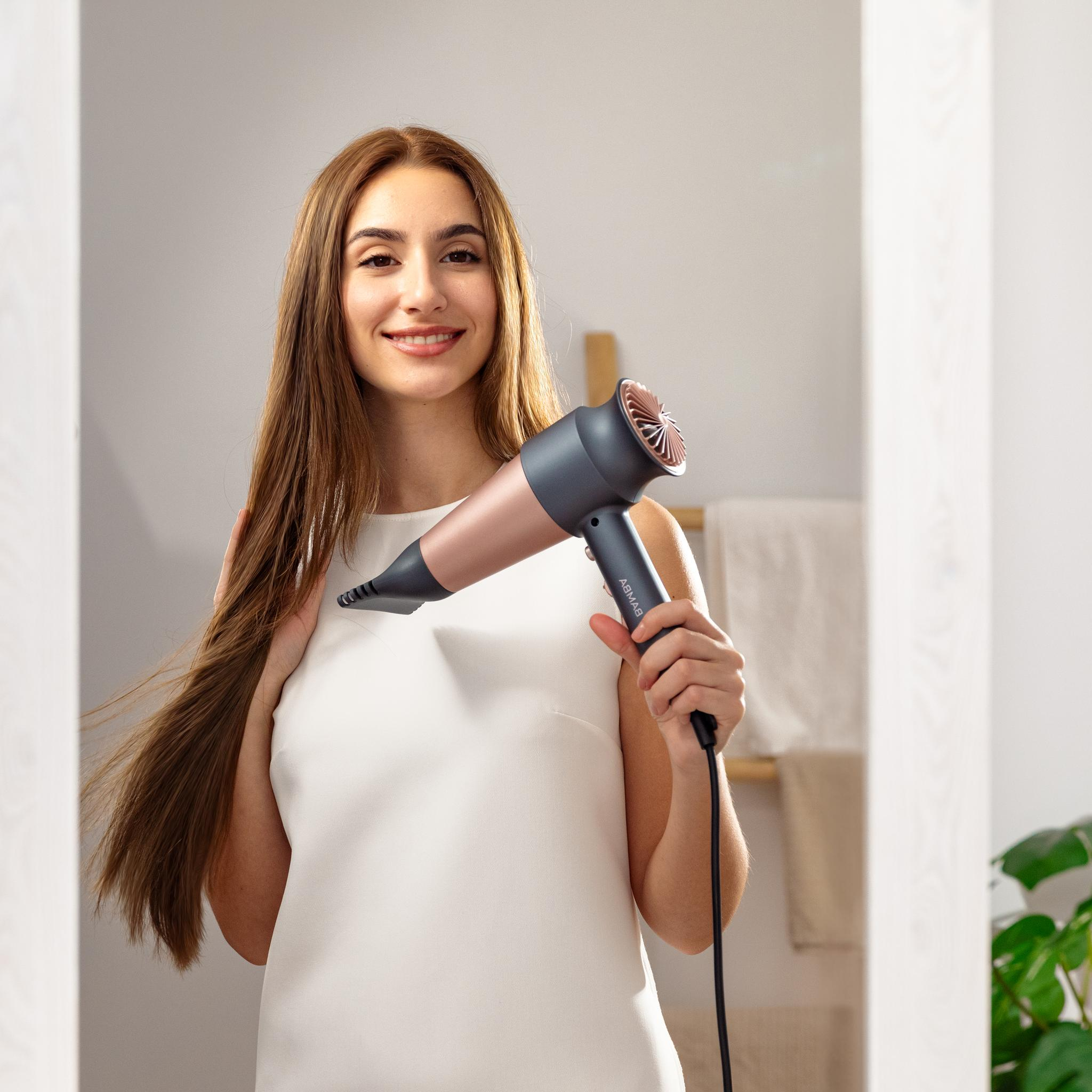 Een vrouw glimlacht terwijl ze een föhn voor een spiegel houdt, haar haar wappert.