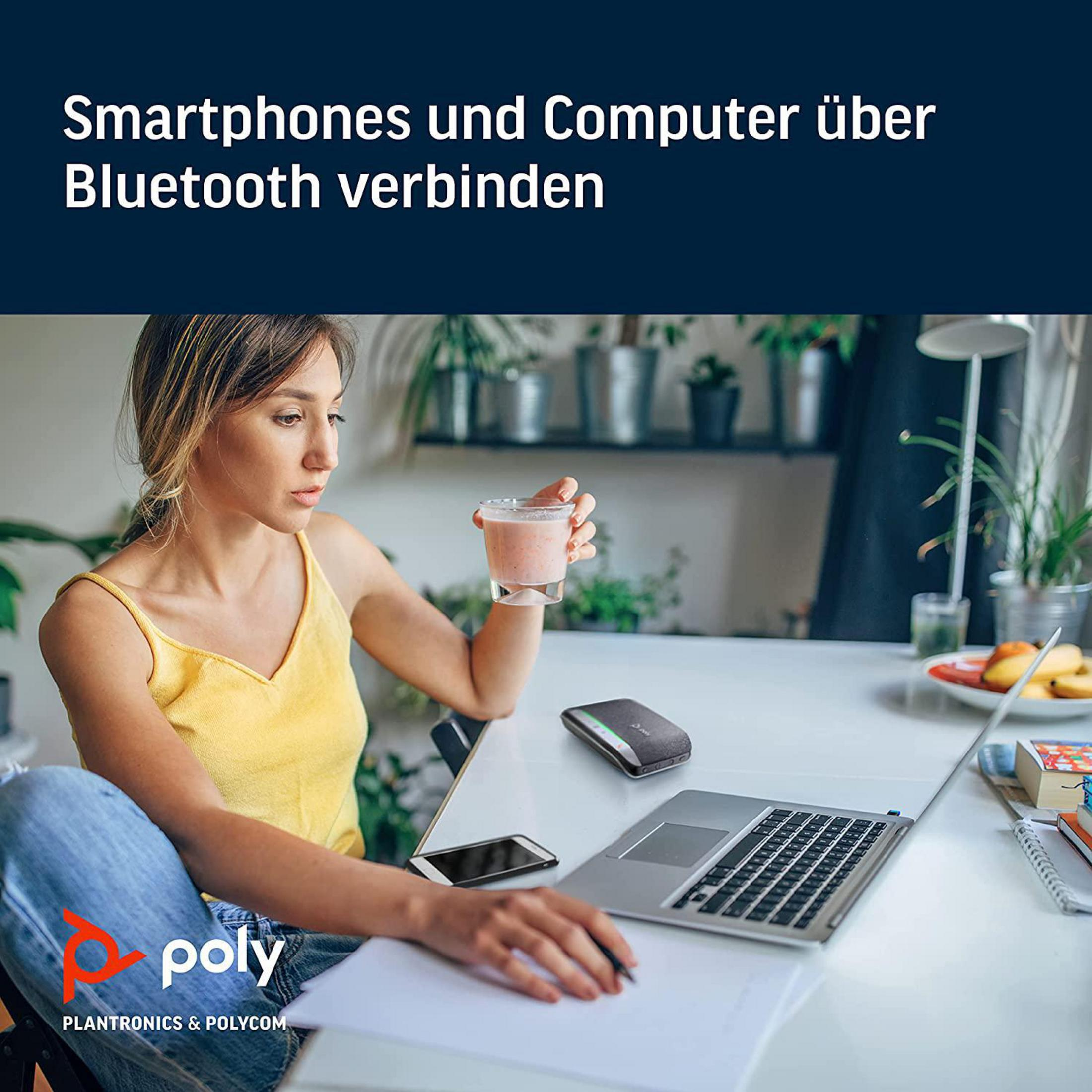 Frau mit Getränk benutzt Laptop, Telefon und Headset auf einem weißen Tisch.