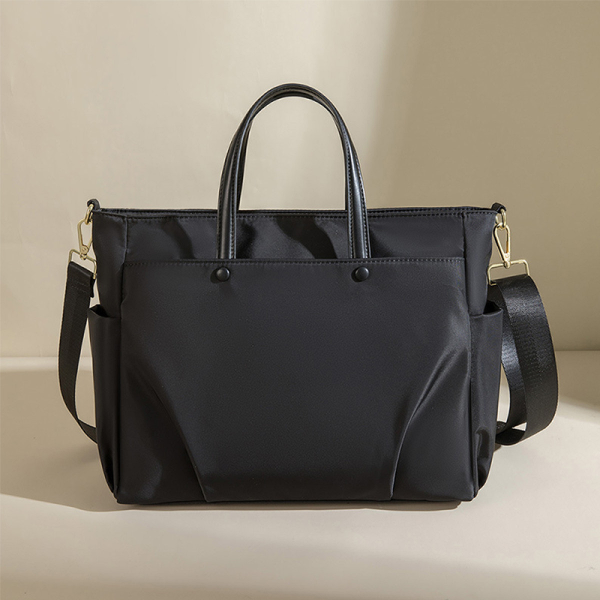 Czarna torba typu tote z paskiem na ramię i wieloma kieszeniami, leżąca na neutralnej powierzchni.