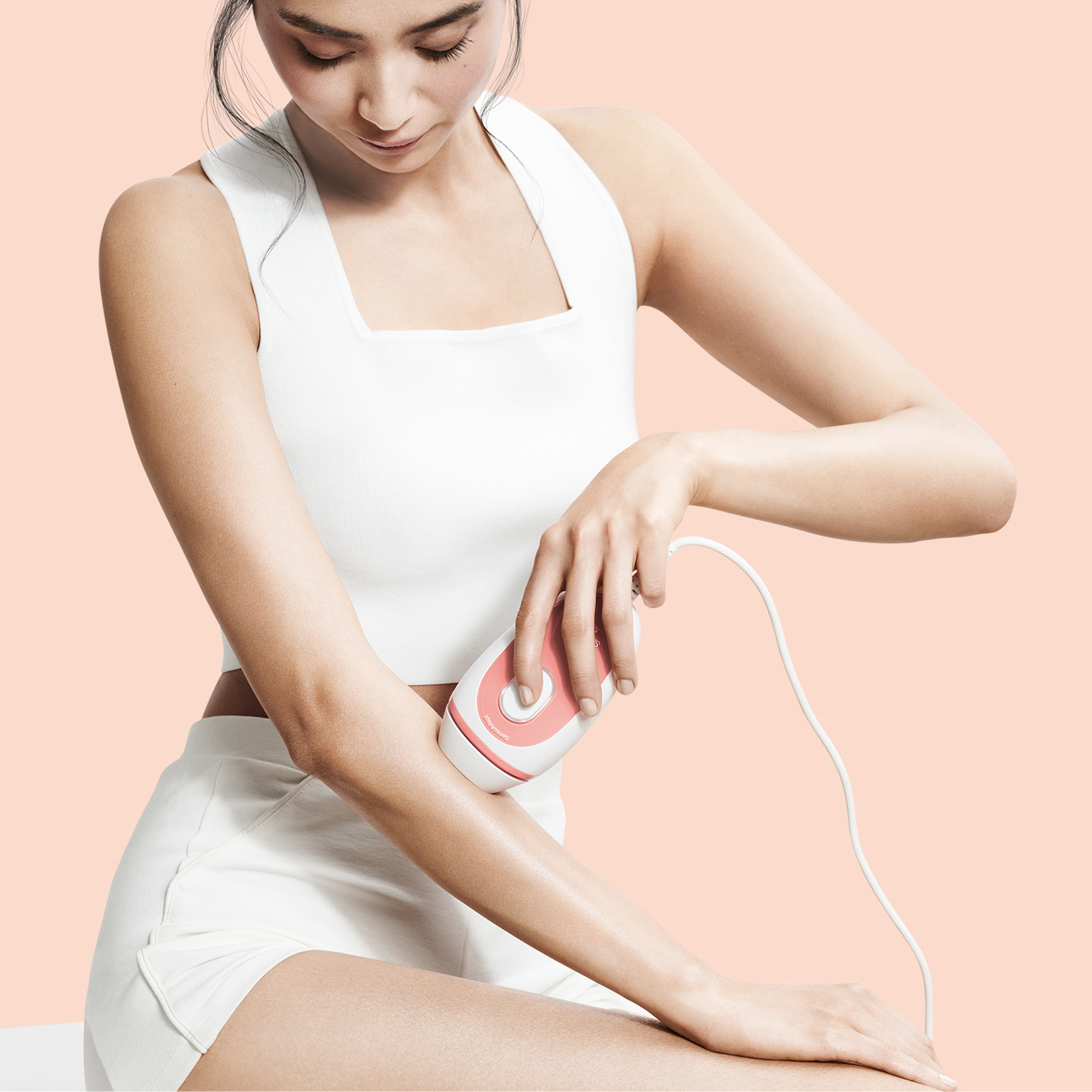 Kobieta używająca różowego depilatora na ramieniu, na brzoskwiniowym tle. Skupienie na urządzeniu.