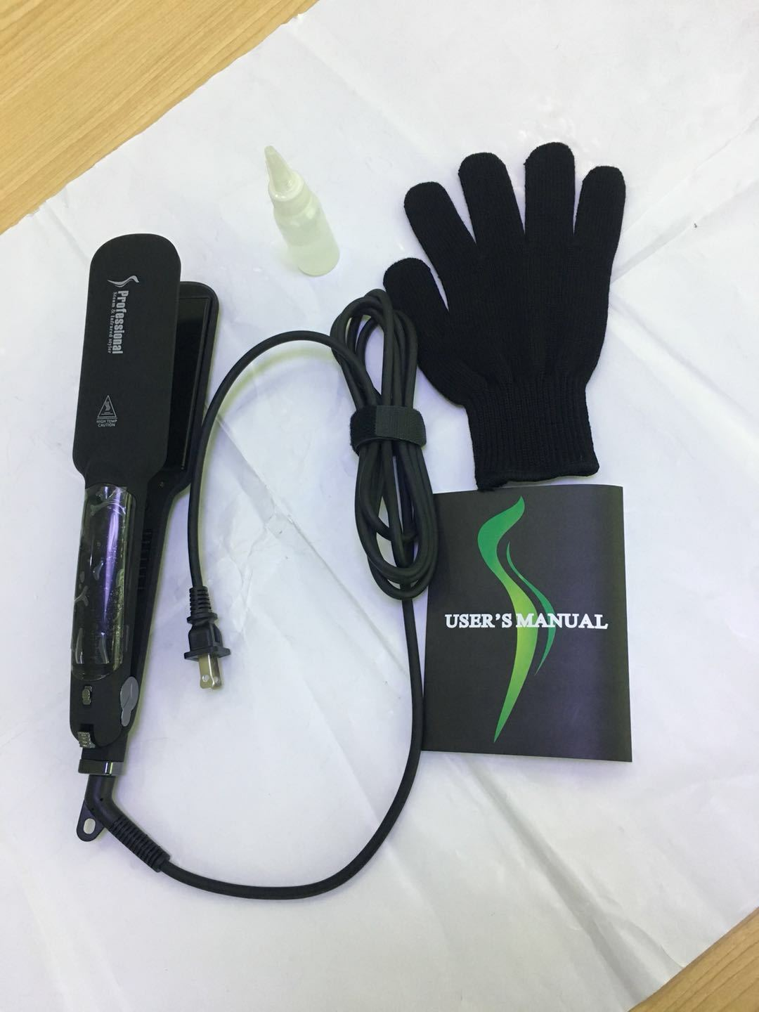Glätteisen und Zubehör, einschließlich eines Handschuhs und einer Bedienungsanleitung, auf weißer Oberfläche.