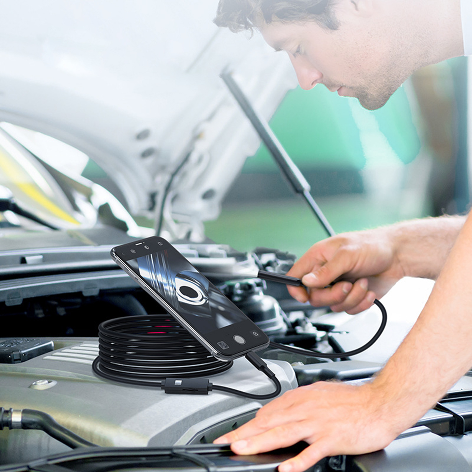 Mann benutzt ein Endoskop, um einen Automotor zu inspizieren. Telefon zeigt Bild. Werkzeuge sichtbar.