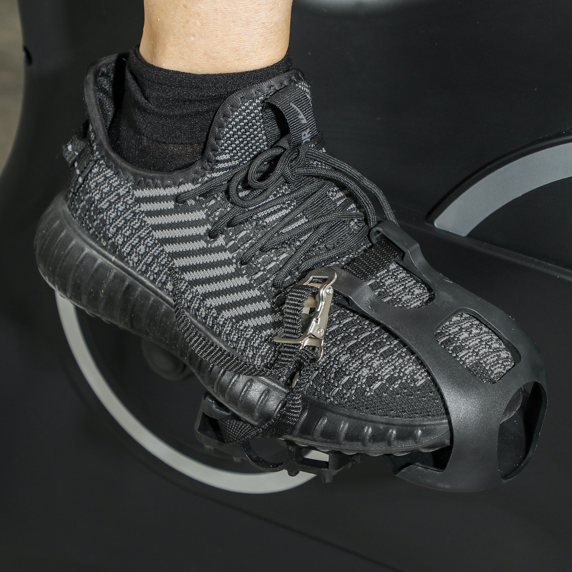 Fuß einer Person in einem schwarz-grauen Sneaker mit einem Fußriemen, der an einem stationären Fahrradpedal befestigt ist.